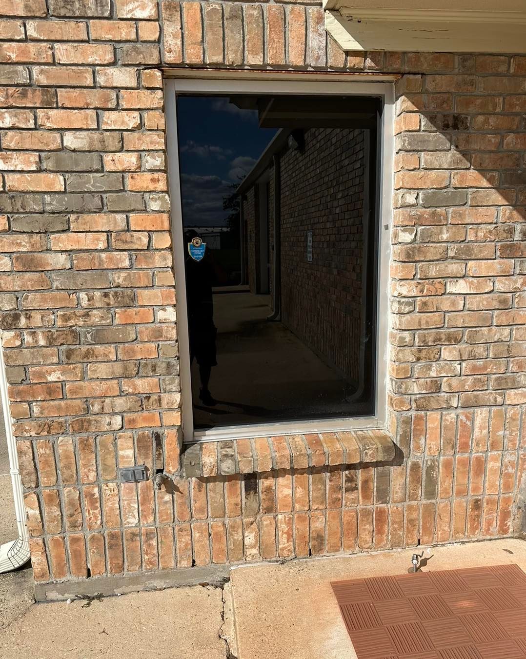A person stands inside a brick building, partially visible through a large, empty, rectangular window frame.