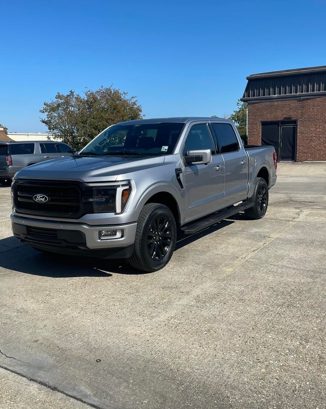 A silver Ford F-150 pickup truck with black wheels and grille parked in an asphalt lot on a sunny day.