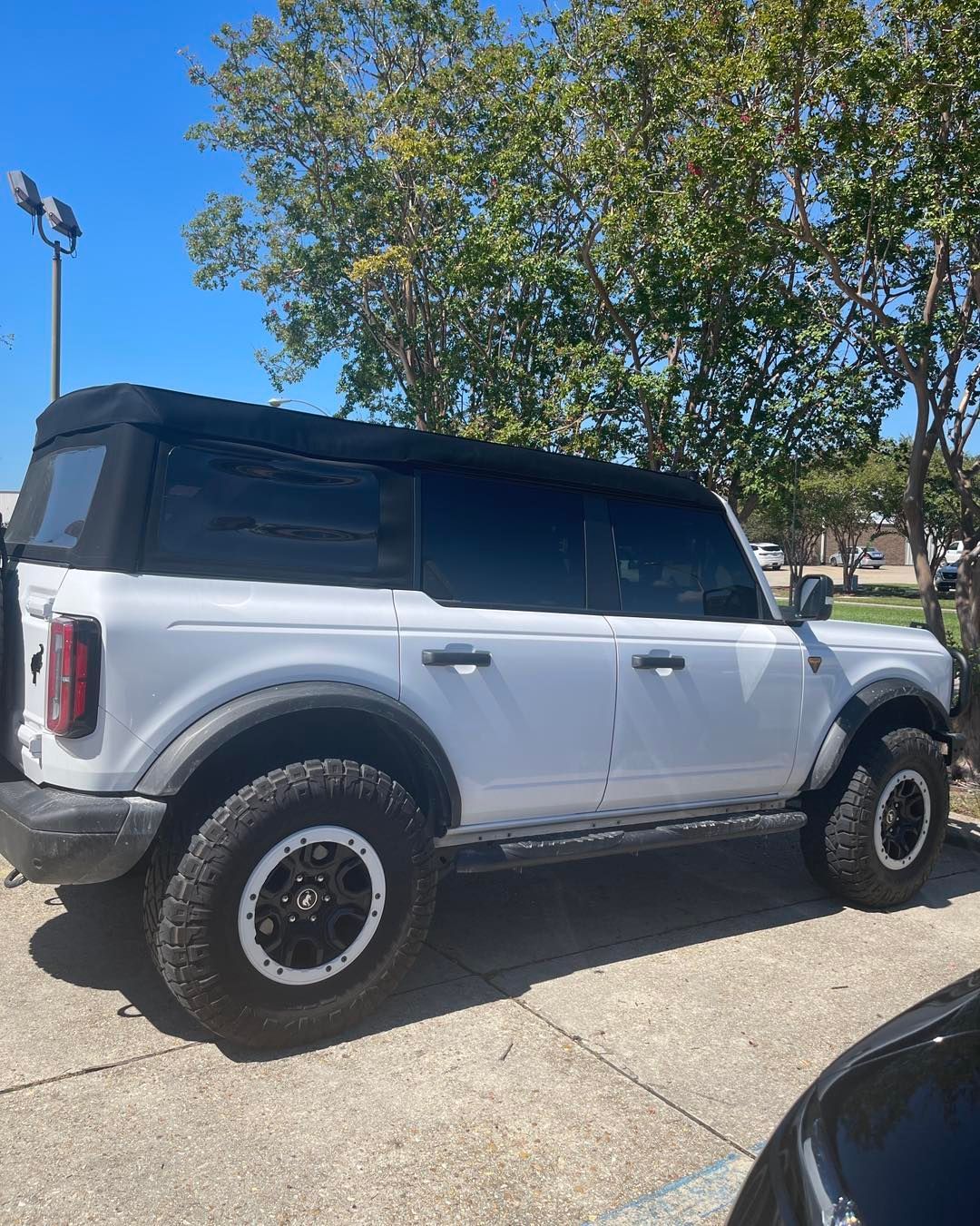 A white four-door Ford Bronco with a black soft top and off-road tires parked on a sunny day.