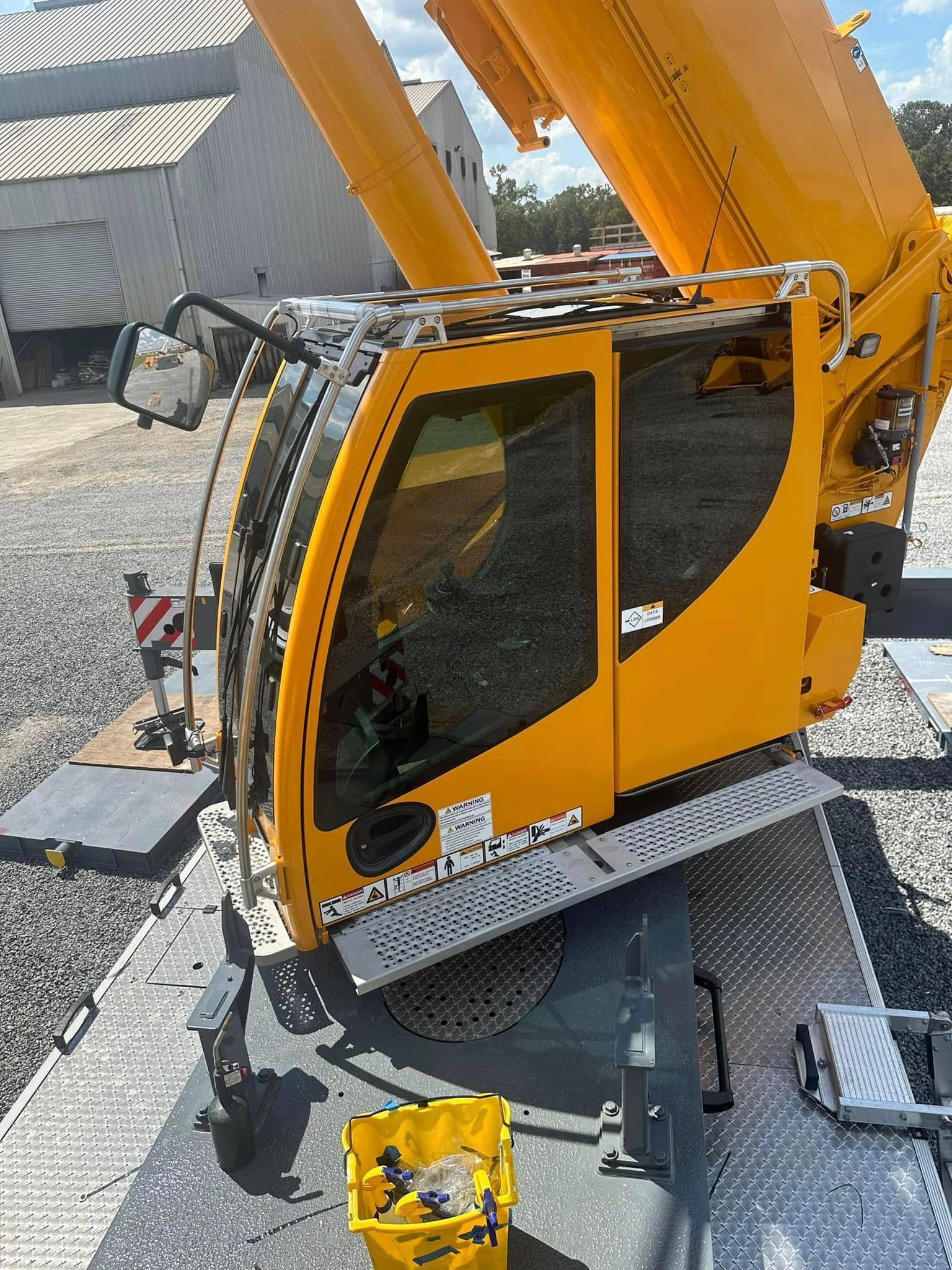 A high-angle view of a bright yellow construction crane cab parked on a gravel surface outdoors.
