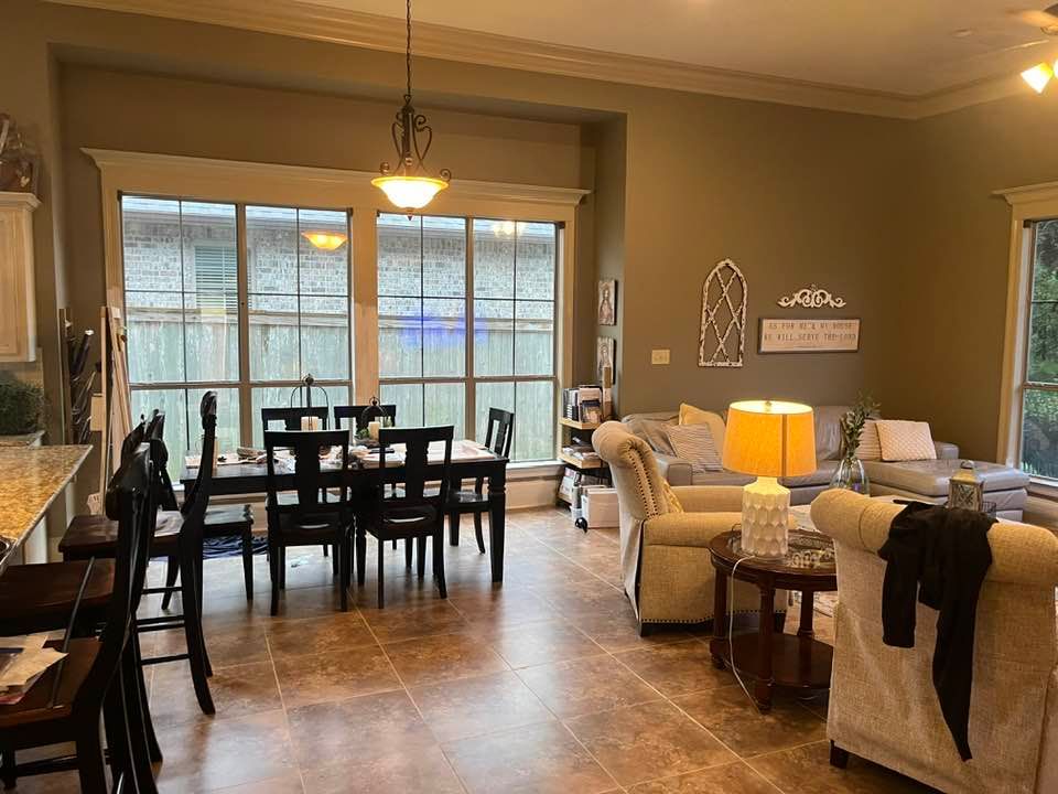 An open-concept dining and living area with a dark wood table, neutral-toned furniture, and large windows.
