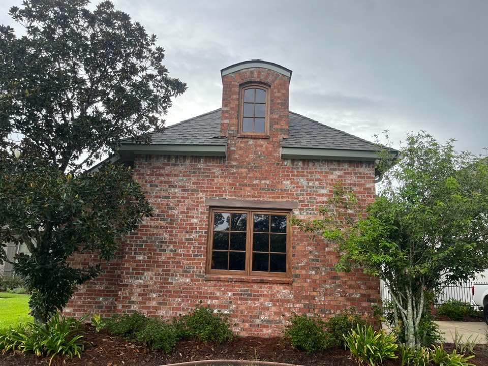 A one-story brick building with a central dormer window and dark-framed windows, surrounded by trees and landscaping.