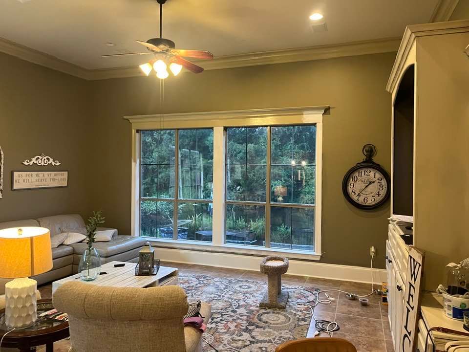 A warm-toned living room features a sectional sofa, a patterned rug, a ceiling fan, and a large round wall clock.