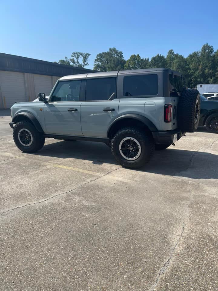A grey four-door Ford Bronco parked on an asphalt lot under a clear blue sky.