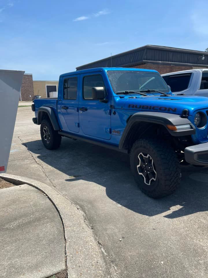 A bright blue Jeep Gladiator Rubicon truck parked on a paved lot under a clear blue sky.