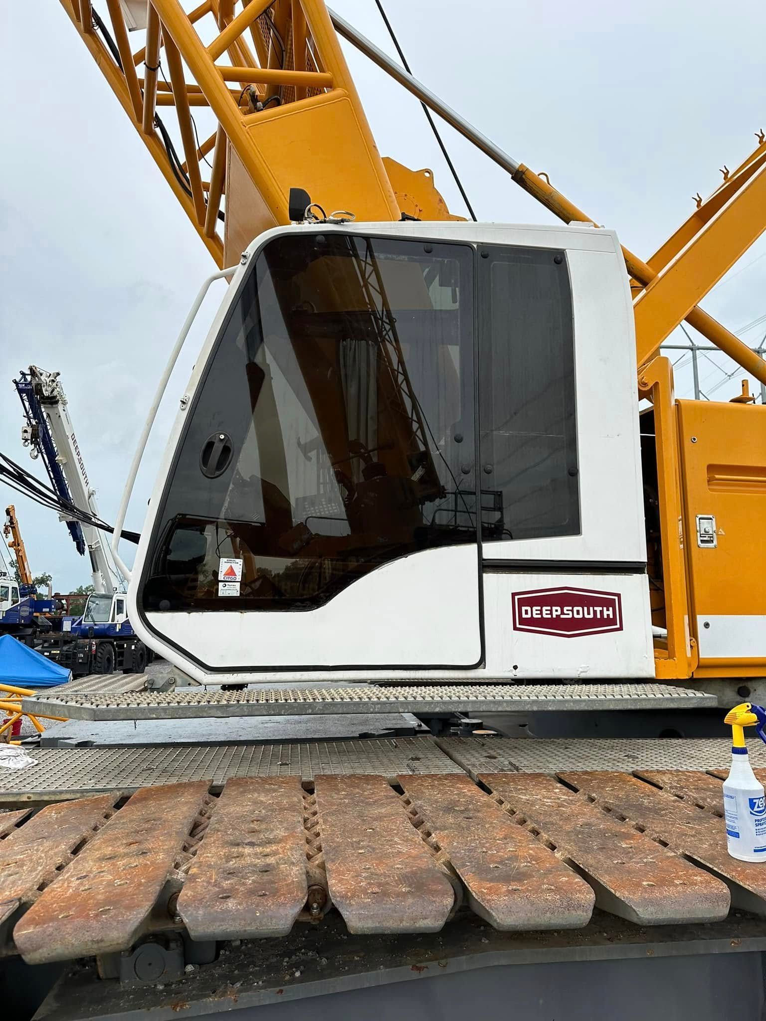 A yellow crane cabin and metal treads on an overcast day, with a small white spray bottle on the side.
