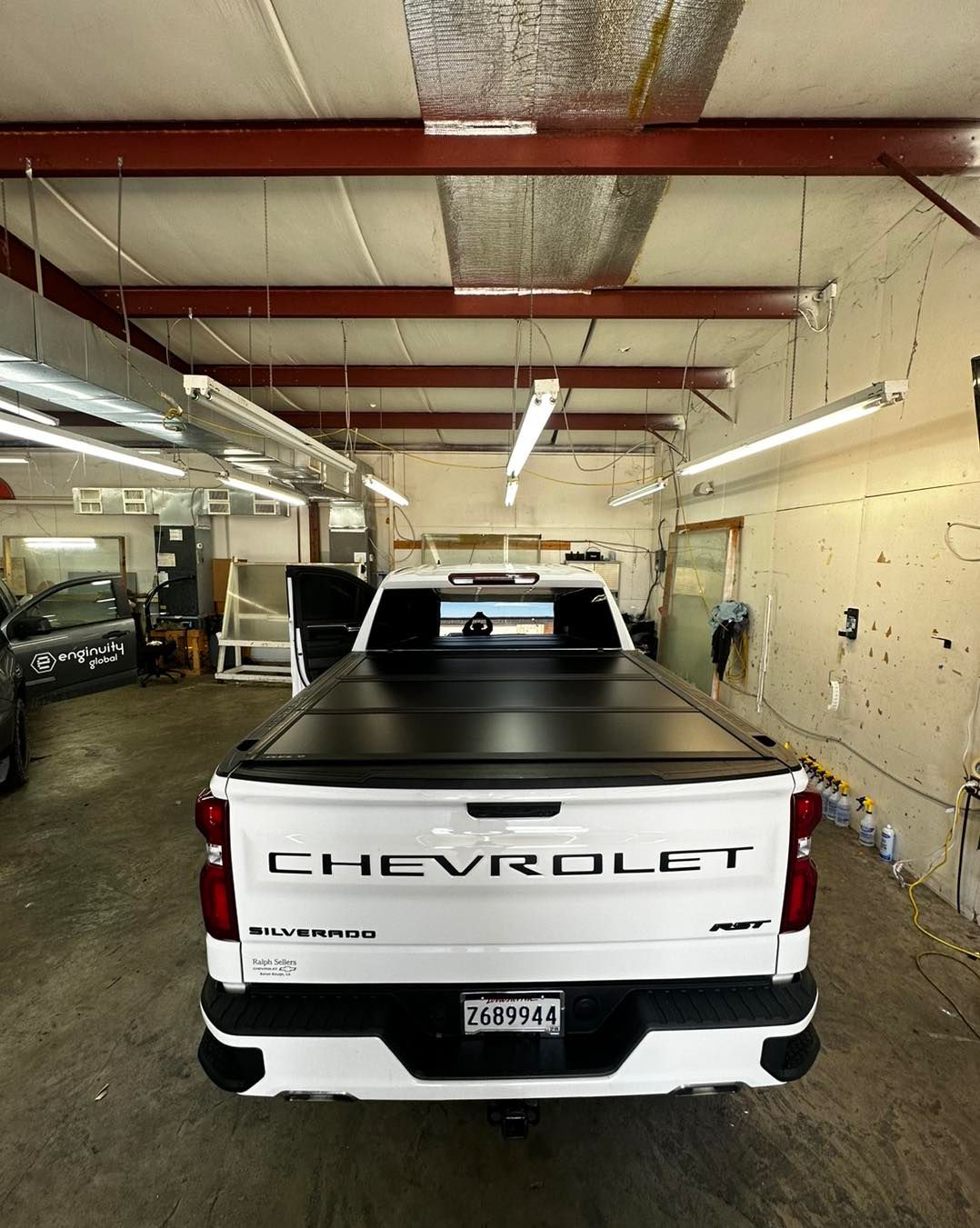 A white Chevrolet pickup truck with a black tonneau cover parked inside an industrial garage.