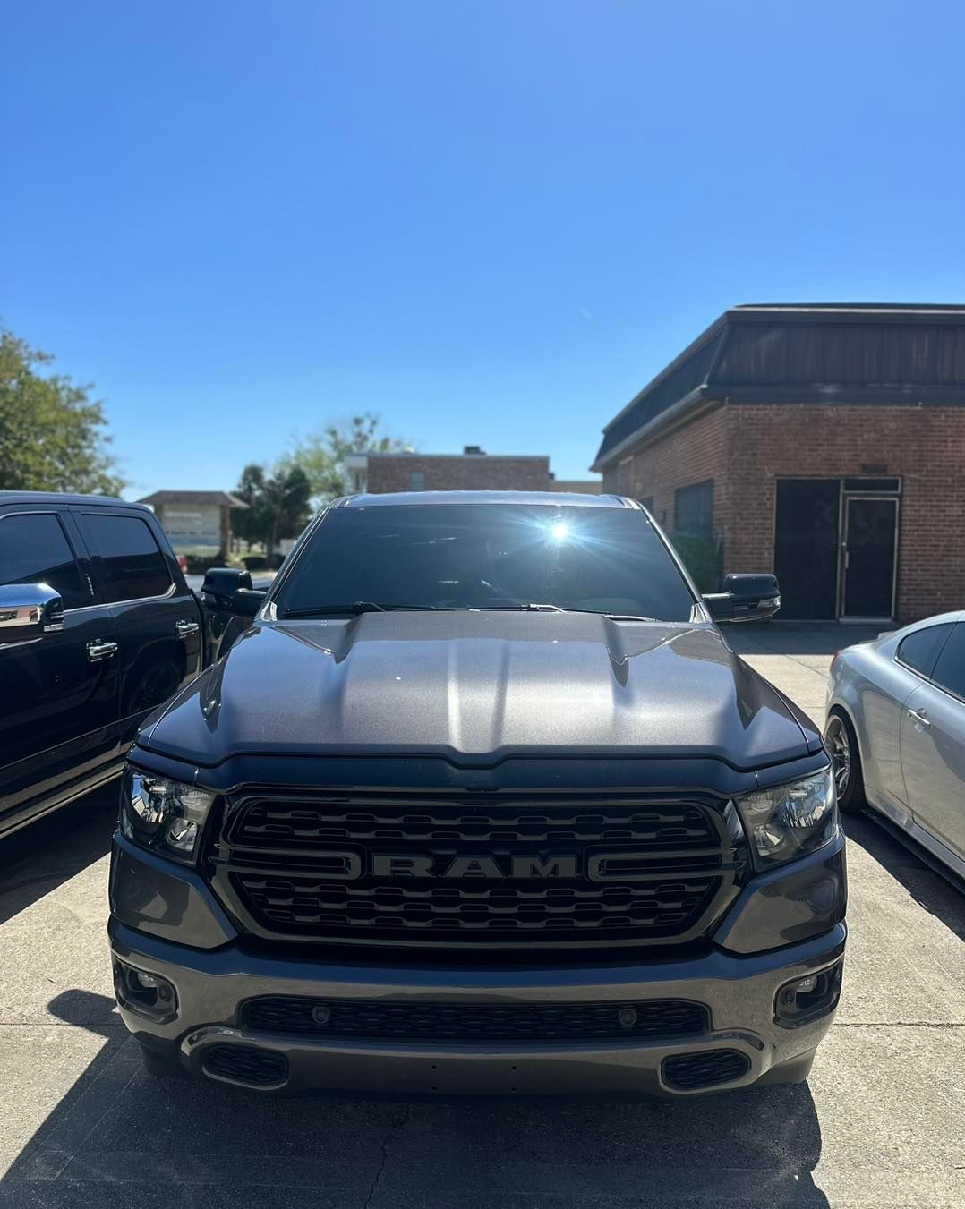 A gray RAM pickup truck parked in a sunny outdoor lot, viewed directly from the front.