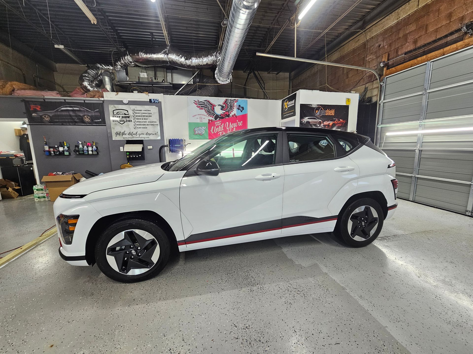 White Hyundai Kona SUV parked inside a garage, black accents, red side stripe, open garage door.