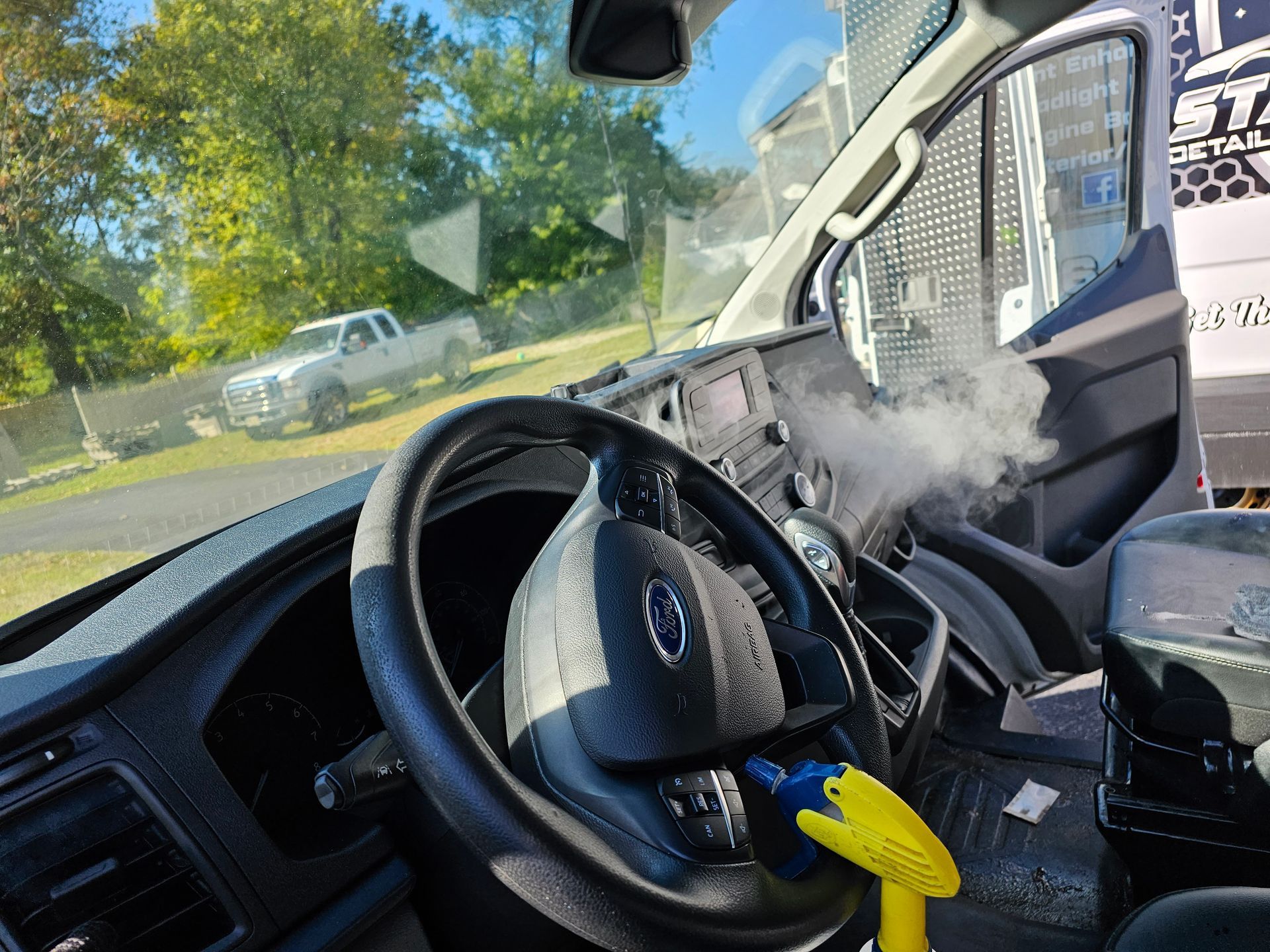 Interior view of a vehicle with steam. Steering wheel, dashboard, and a utility truck visible through the windshield.