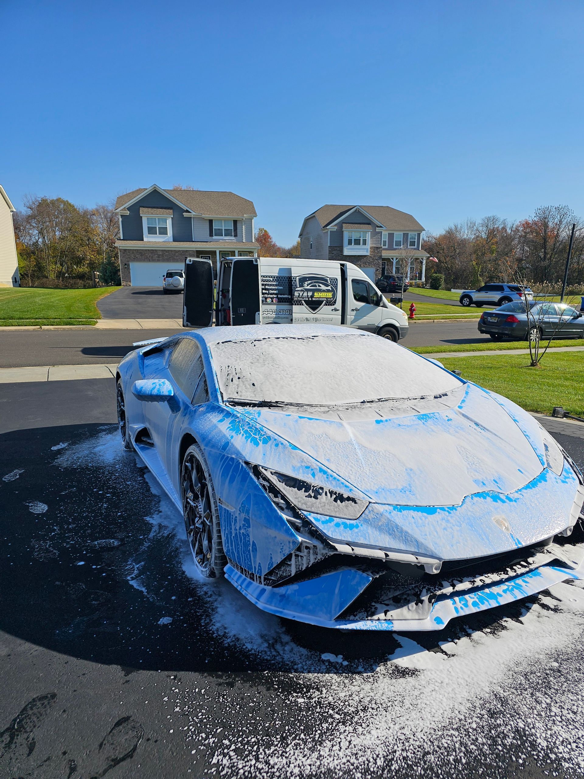 Blue Lamborghini covered in soapy foam, parked in driveway during wash.