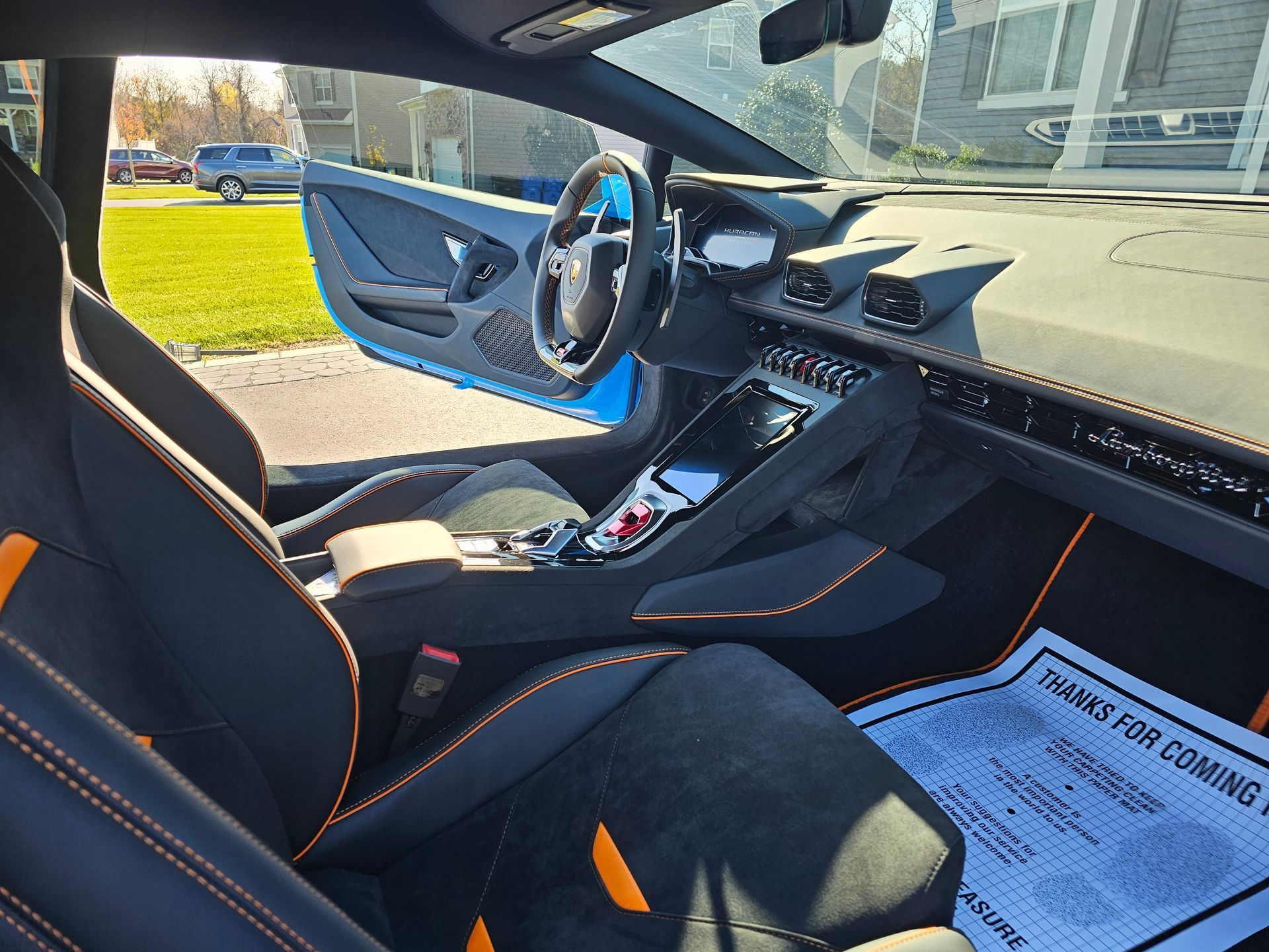Interior of a blue Lamborghini sports car with black and orange accents. Open driver's side door, sunlight.