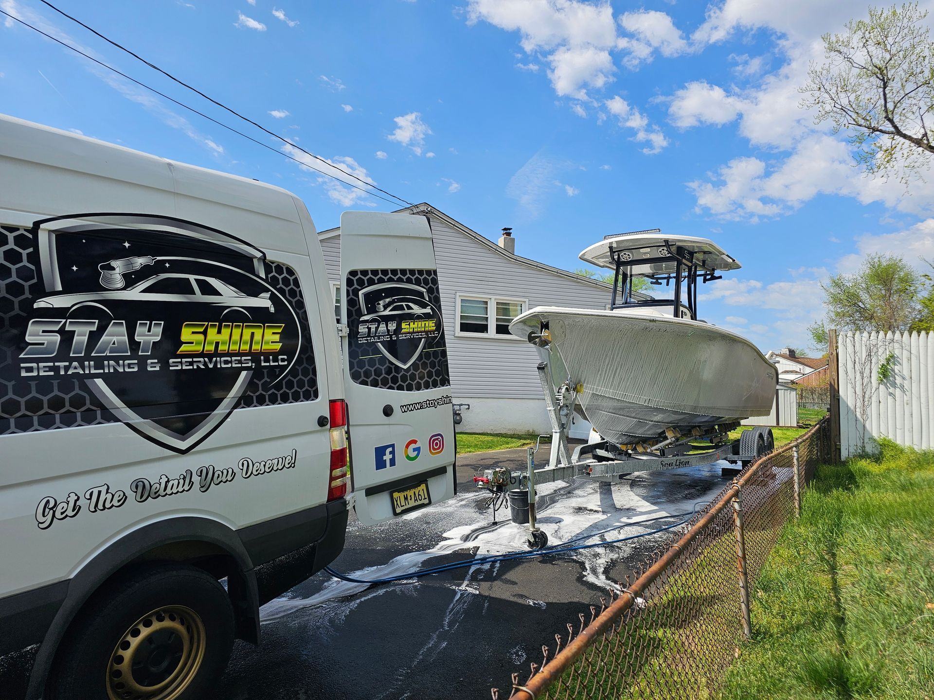 Boat being washed with foam by a van, sunny outdoor setting.