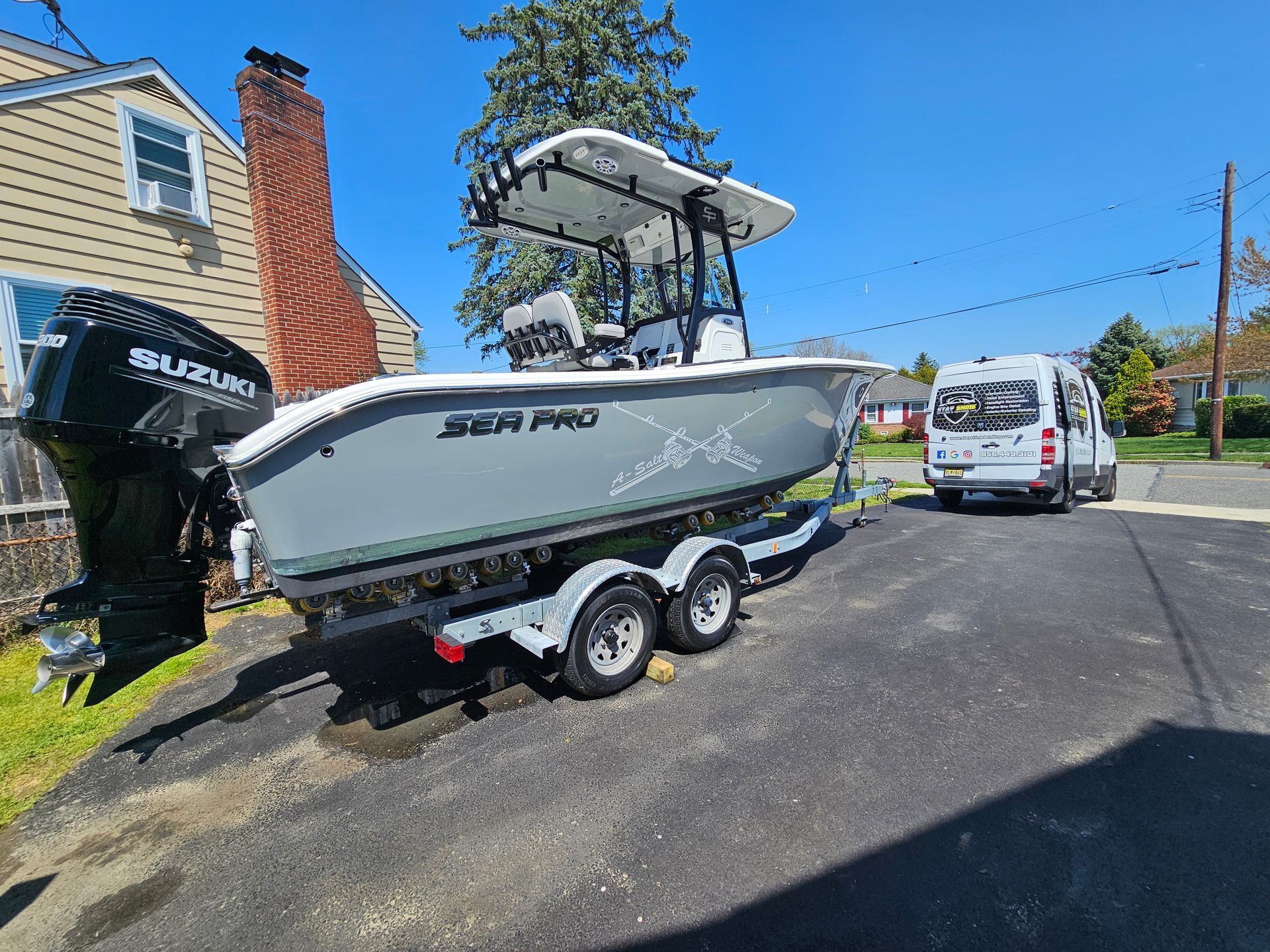 Gray and white fishing boat on a trailer, parked on a driveway in front of a house, Suzuki outboard motor.