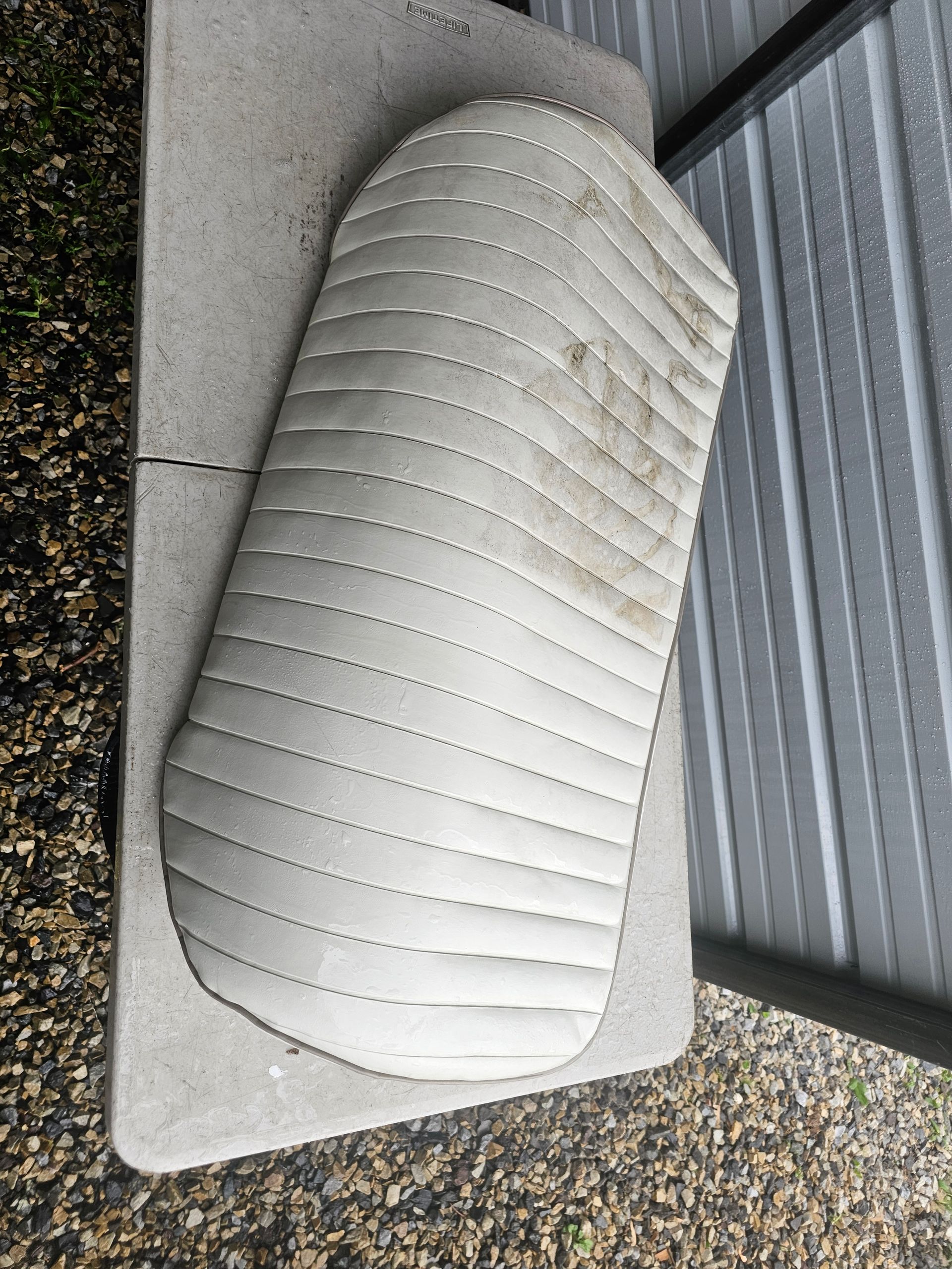 Gray quilted seat cushion on a light gray surface, against a corrugated metal wall.