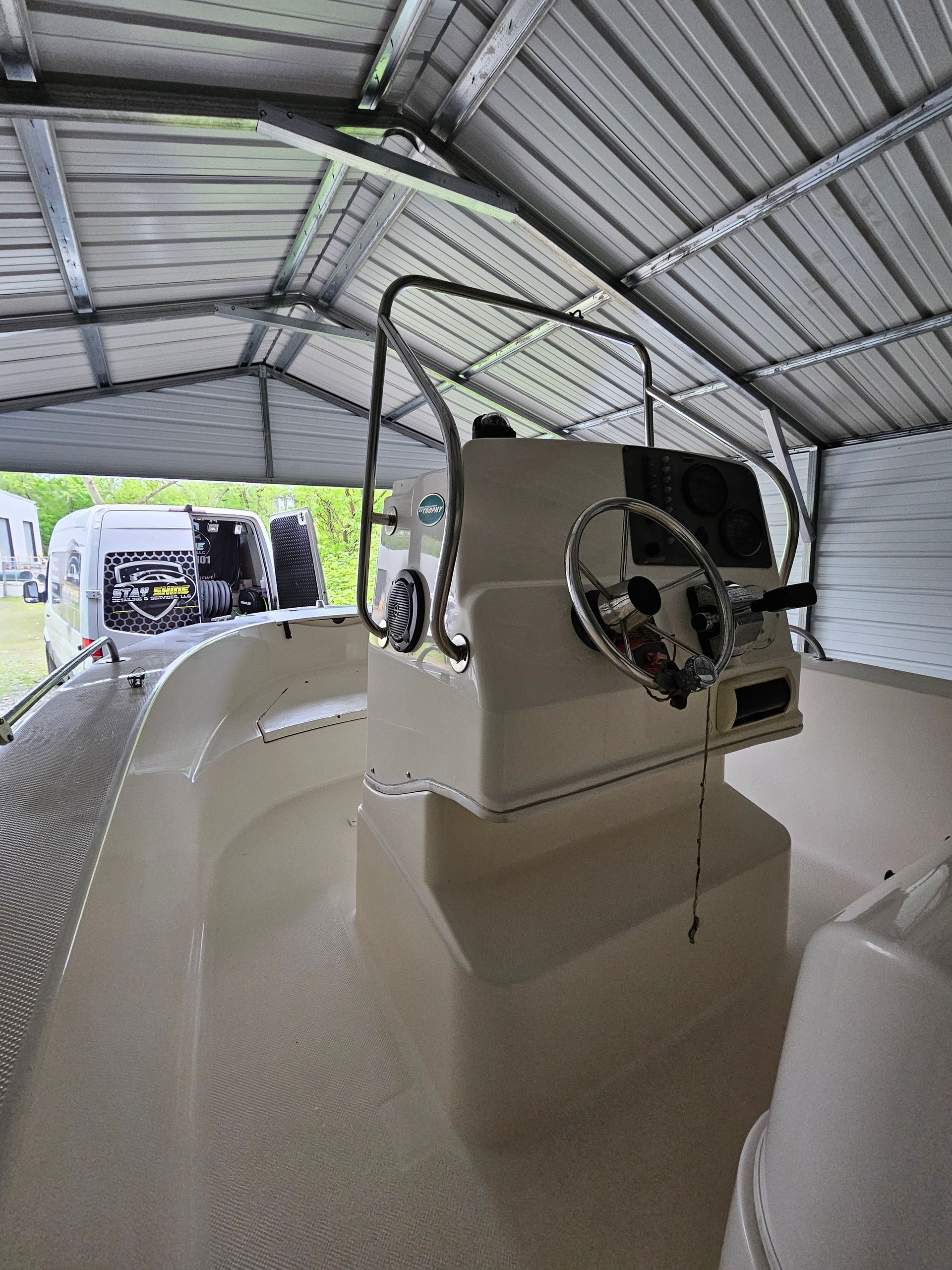 Interior view of a white boat, showing the helm with a steering wheel under a metal shelter.