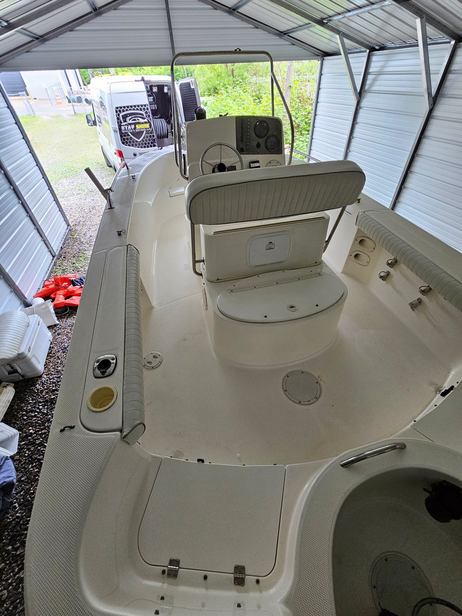 Boat interior under a metal shelter. Light beige interior, console, and white seats.