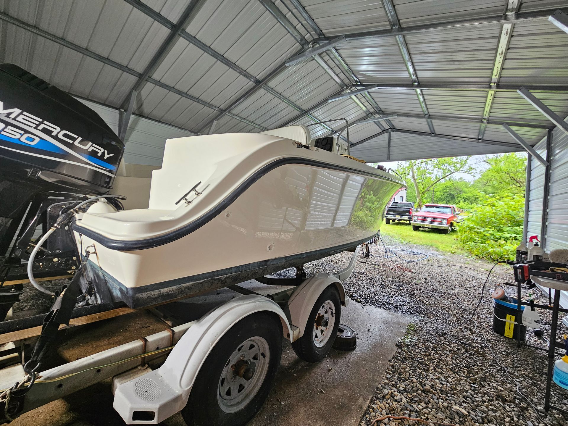 Boat on trailer under metal shed with Mercury 250 engine.