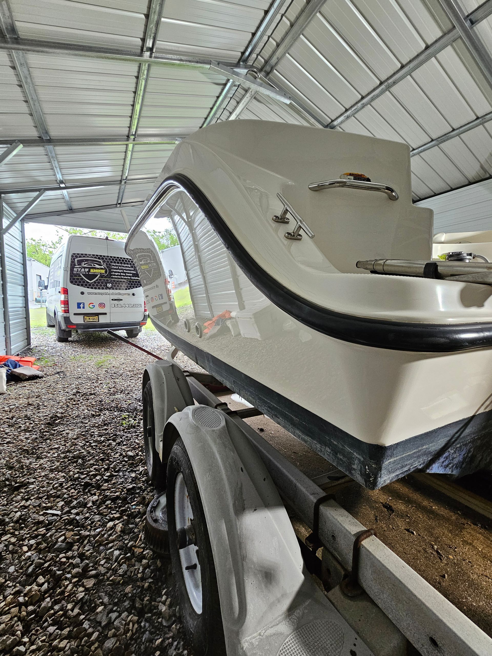 Boat on a trailer under a metal roof, next to a van.