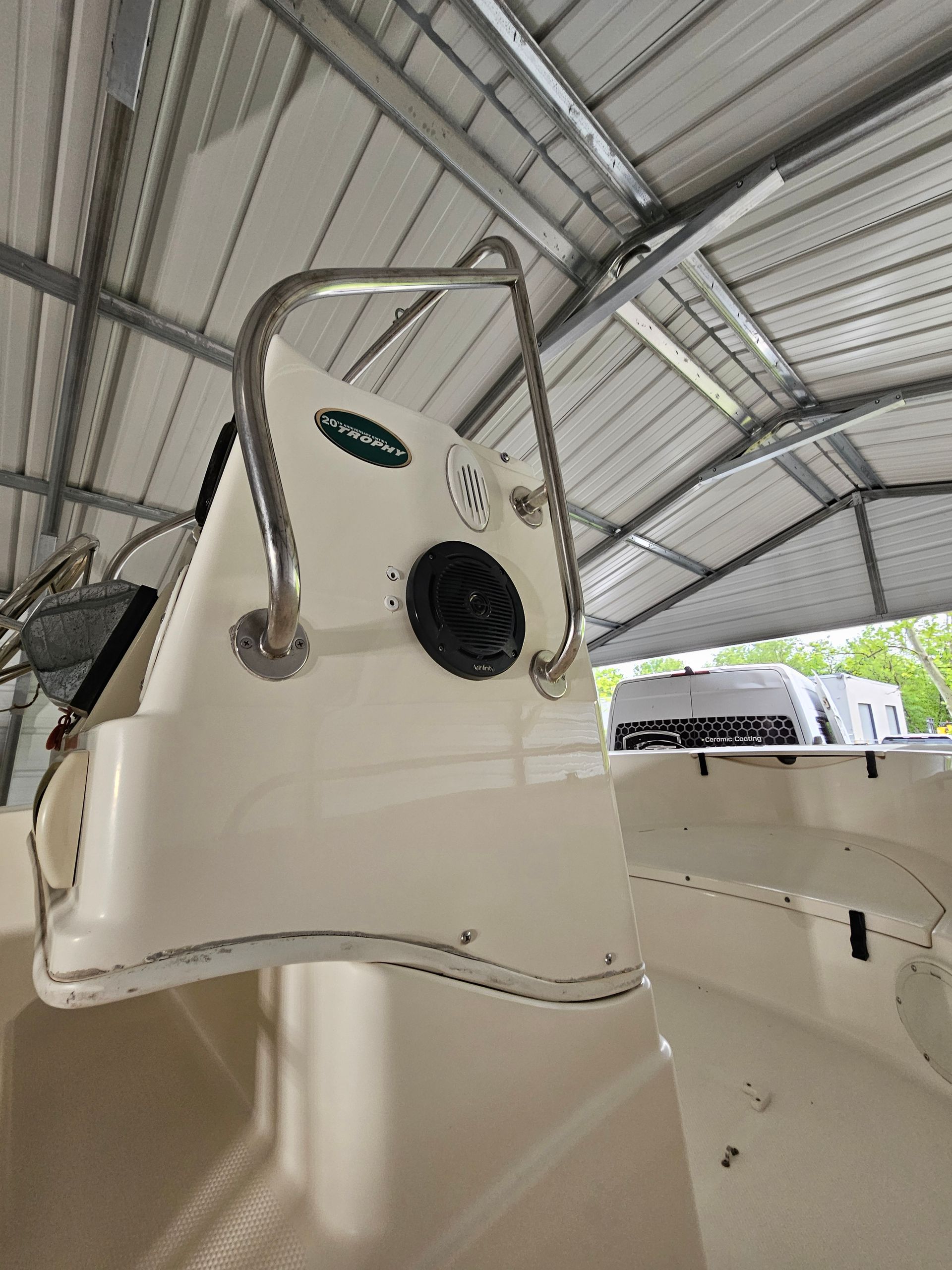 Boat console with stainless steel grab bar, speaker, and gauges, under a metal roof.