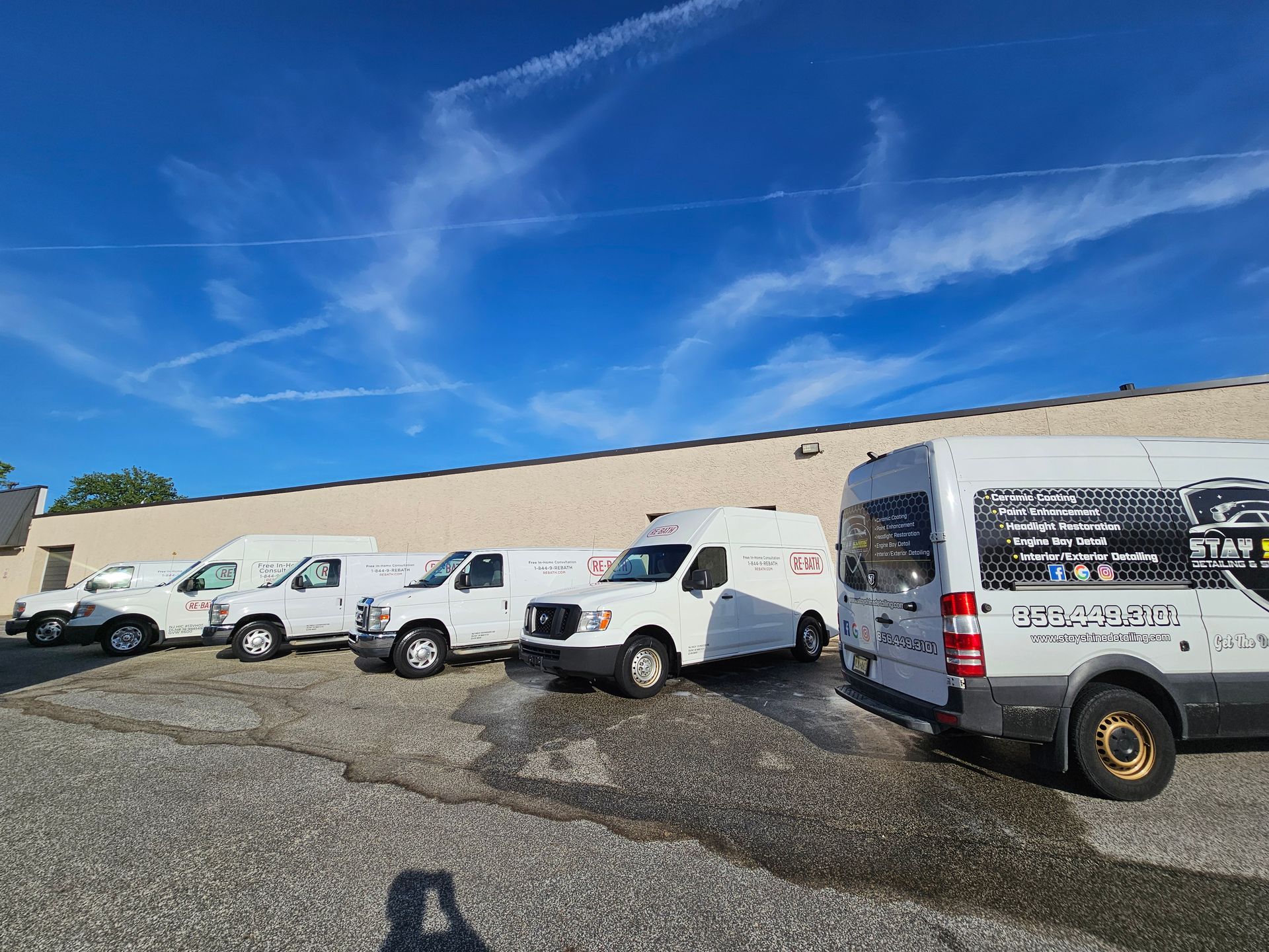 A row of white service vans parked outside a building on a sunny day.