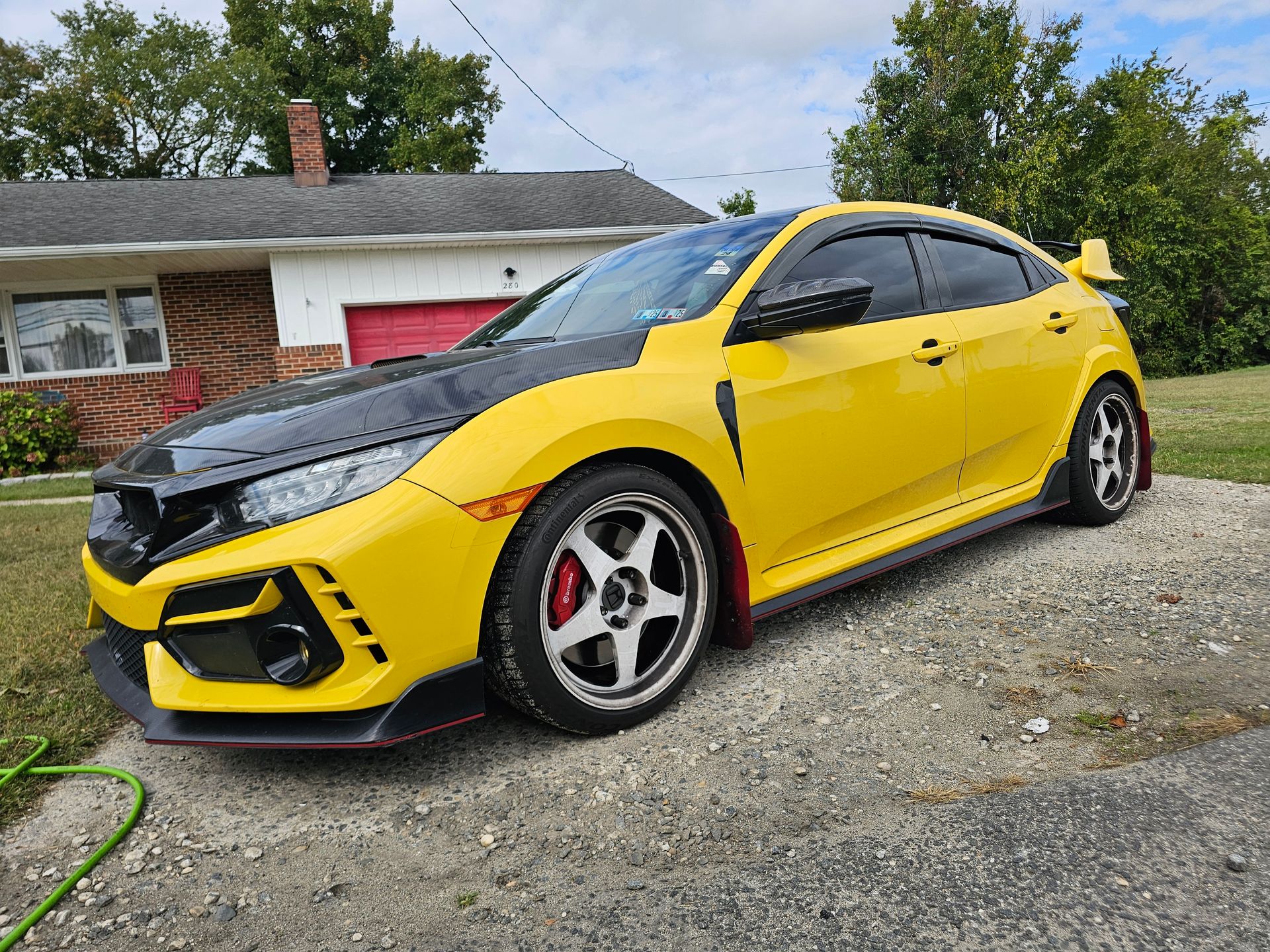 Yellow and black Honda Civic Type R parked on gravel driveway.