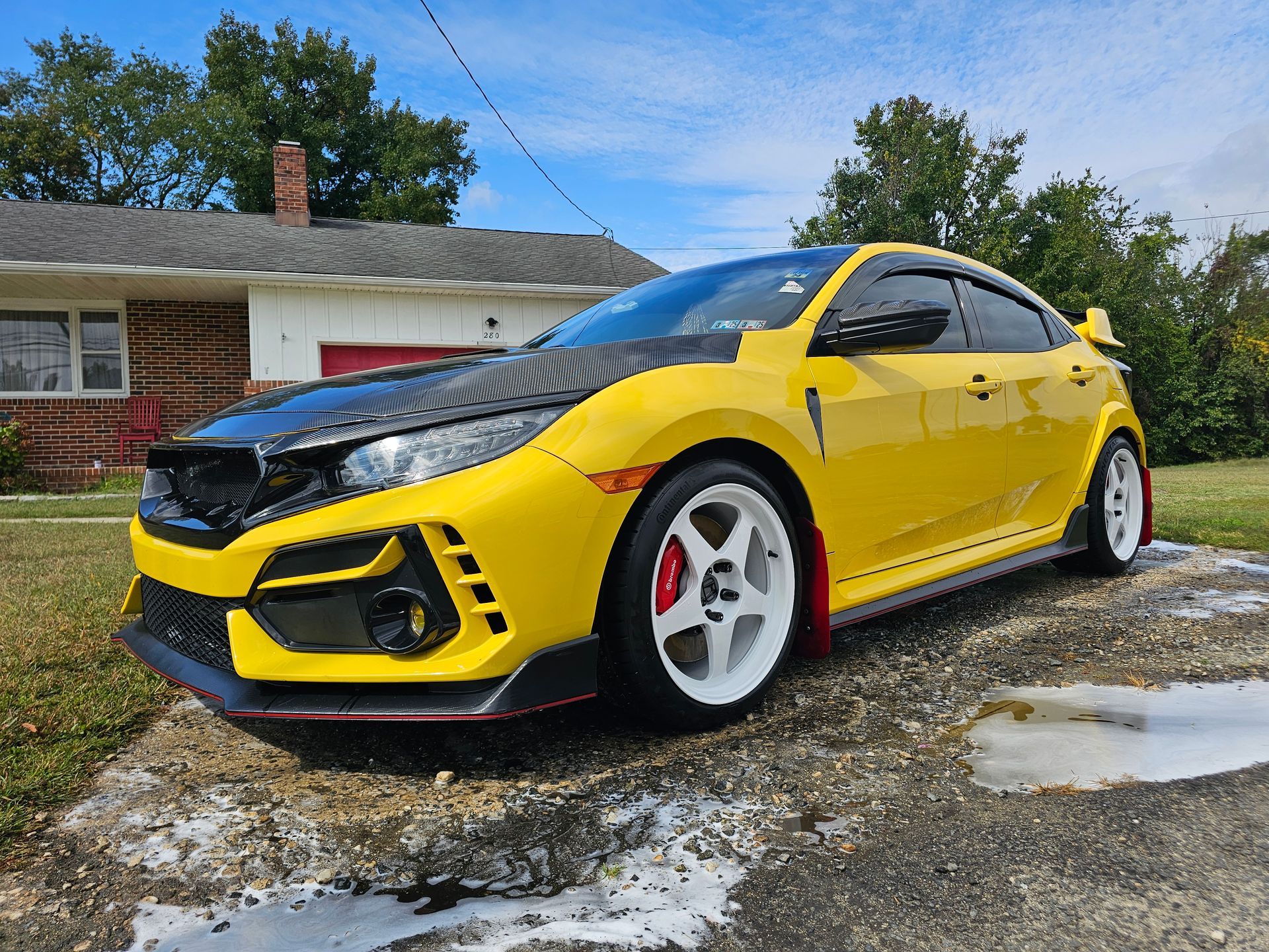 Yellow Honda Civic Type R with a black hood, parked in front of a house on a sunny day.