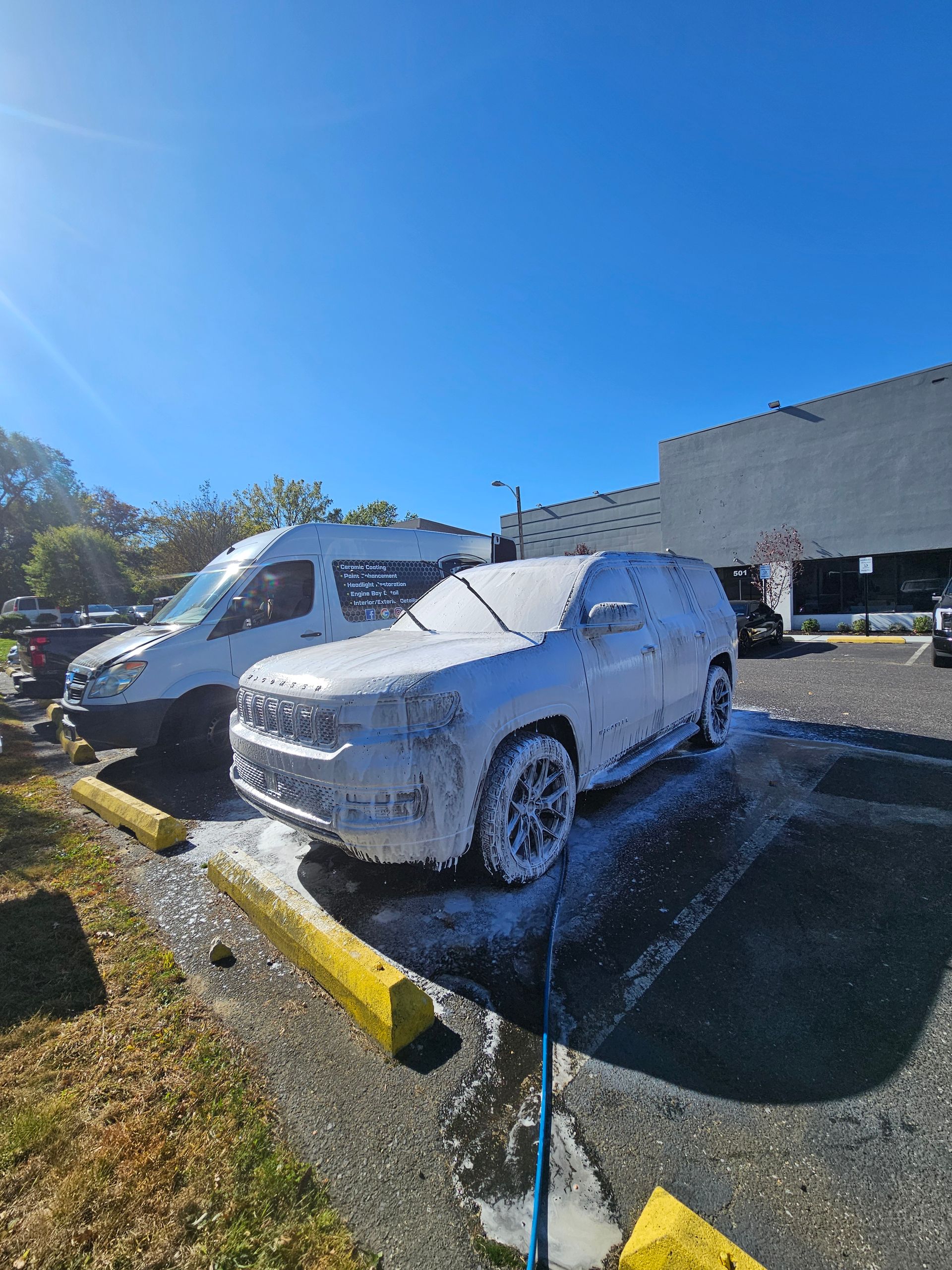 SUV and van covered in white foam, parked near a building on a sunny day.