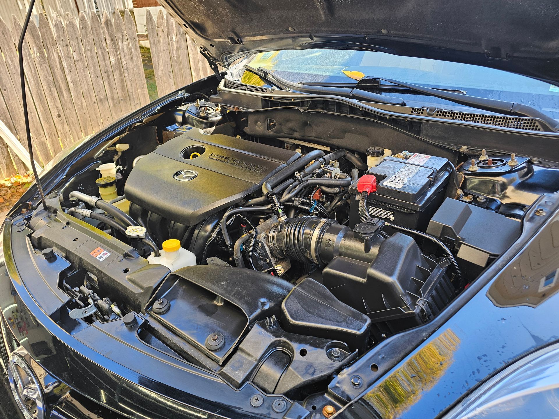 Black car engine bay with the hood open, showing the engine and components.