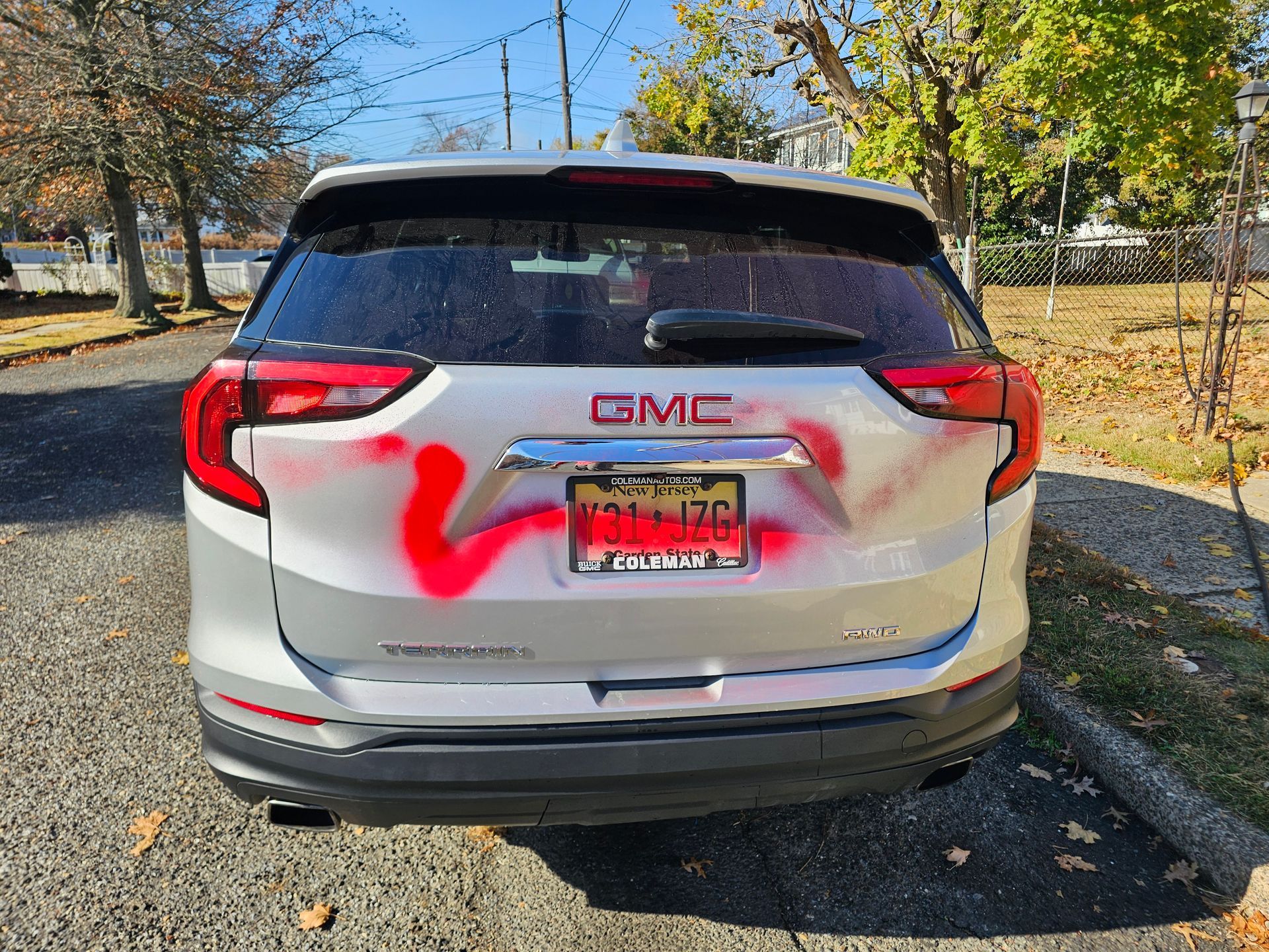 Silver GMC SUV vandalized with bright pink spray paint on the rear window and trunk in an outdoor setting.