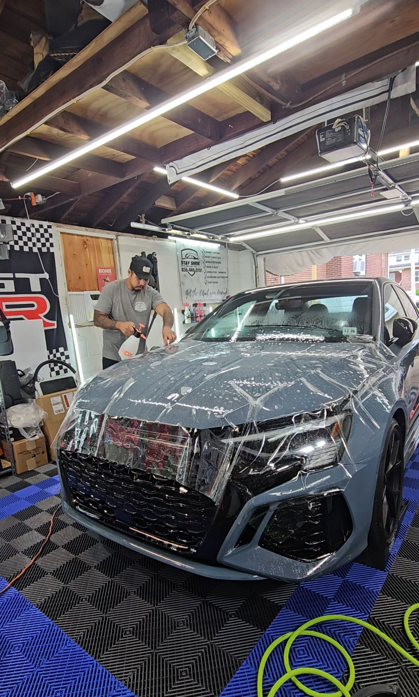 Man washing a gray car in a garage with neon lights.