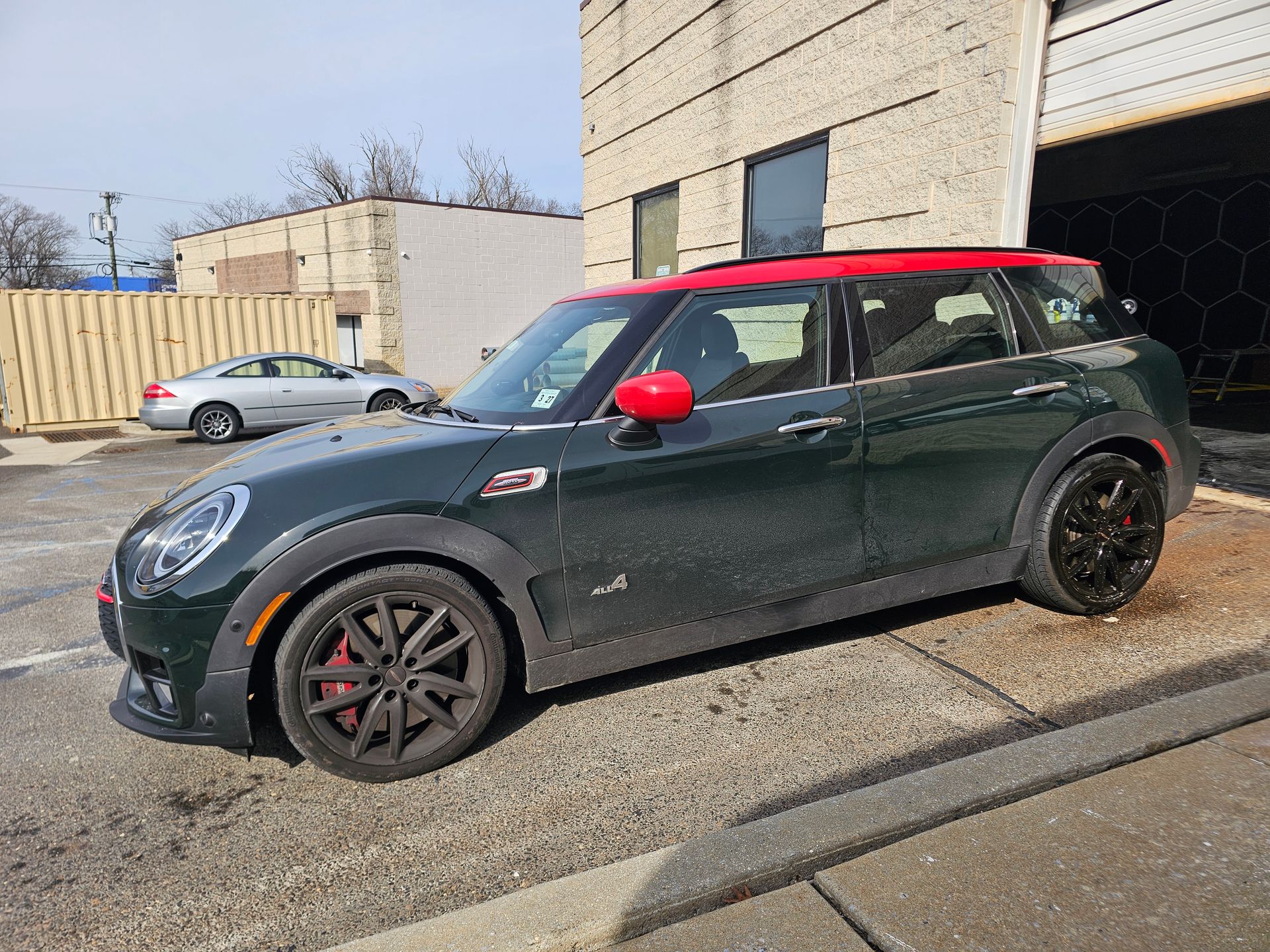 Green Mini Cooper Clubman with a red roof, parked outside a building.