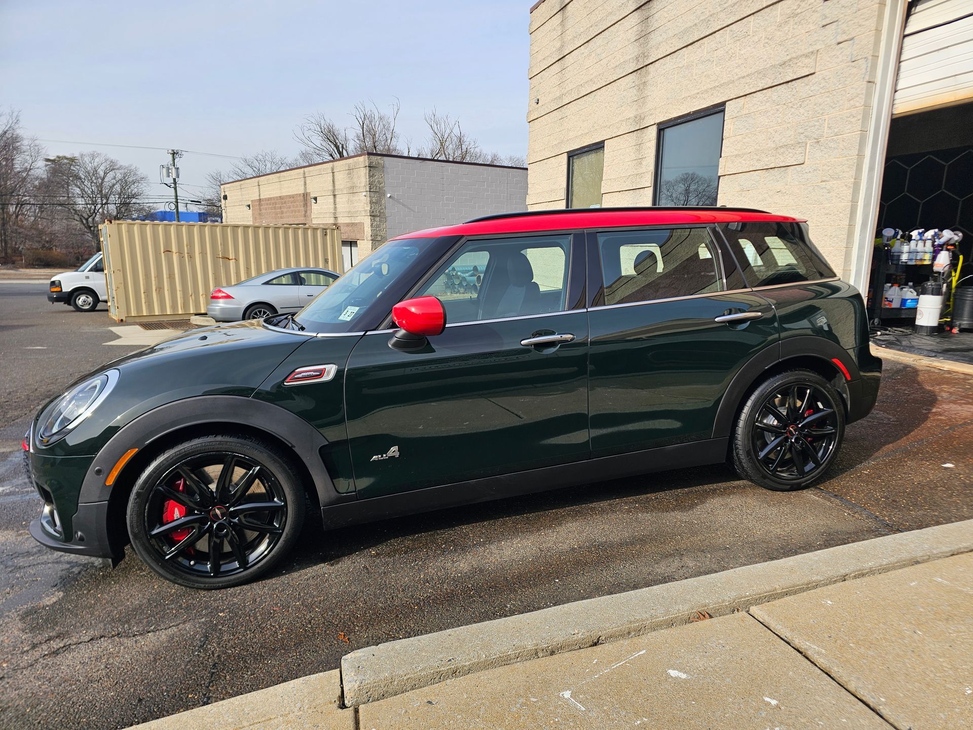 Green Mini Cooper Clubman with a red roof and side mirror caps, parked next to a building.