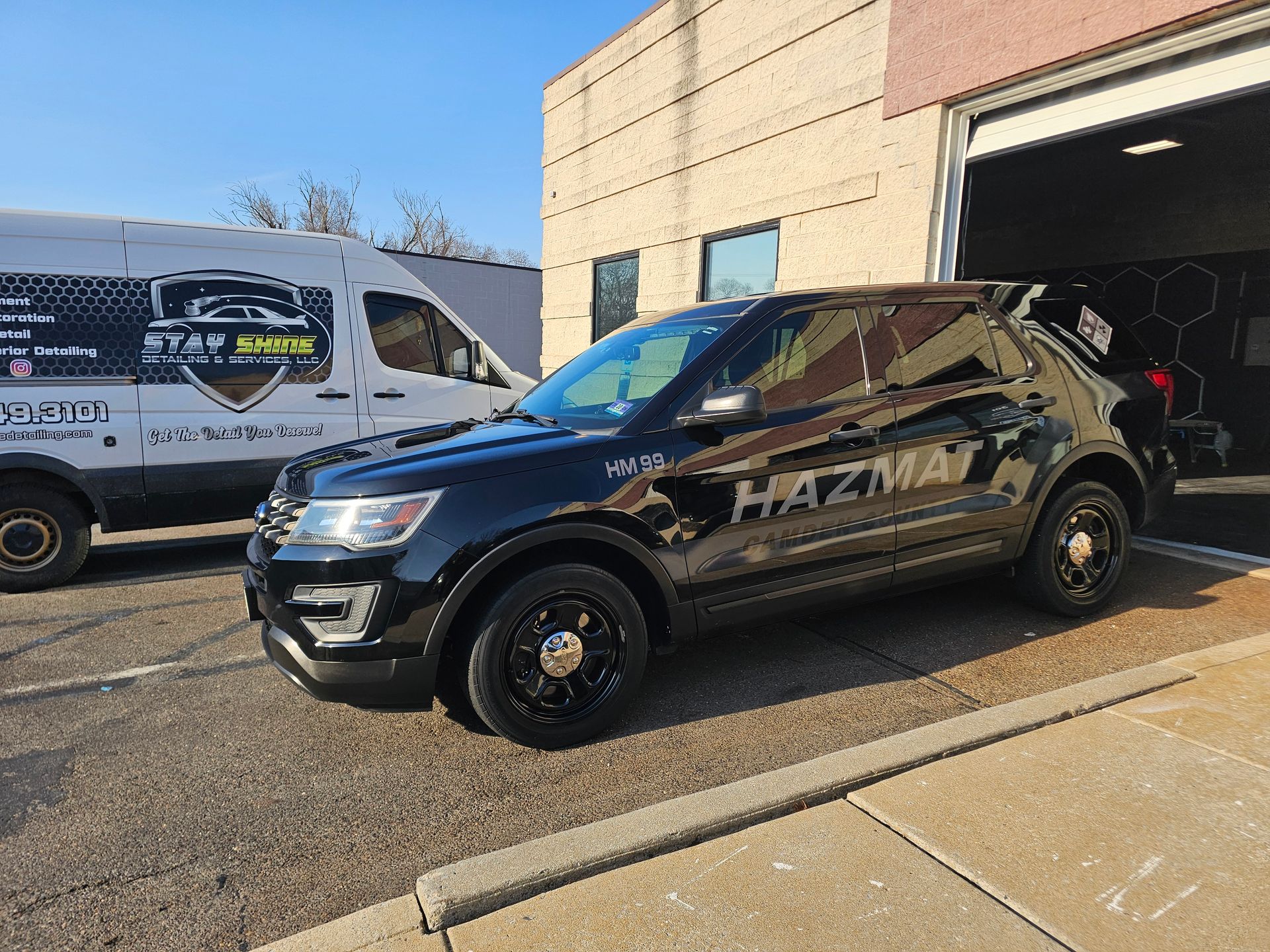 Black HAZMAT vehicle parked outside a building, with a HAZMAT van visible behind it.