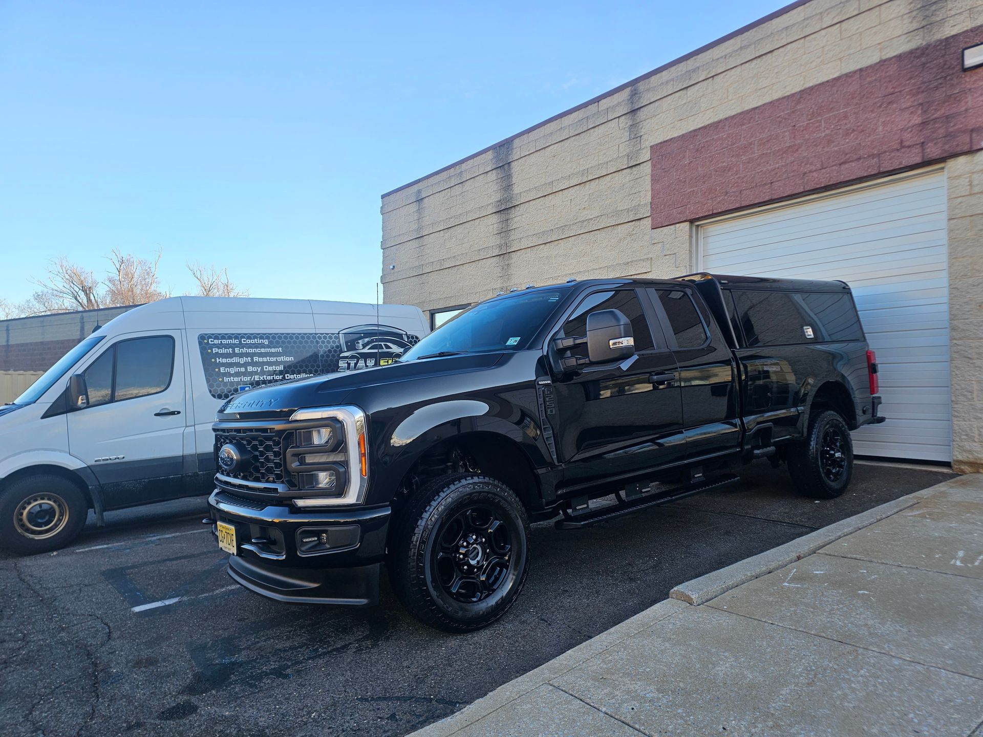 Black pickup truck parked outside a building, next to a white van on a sunny day.