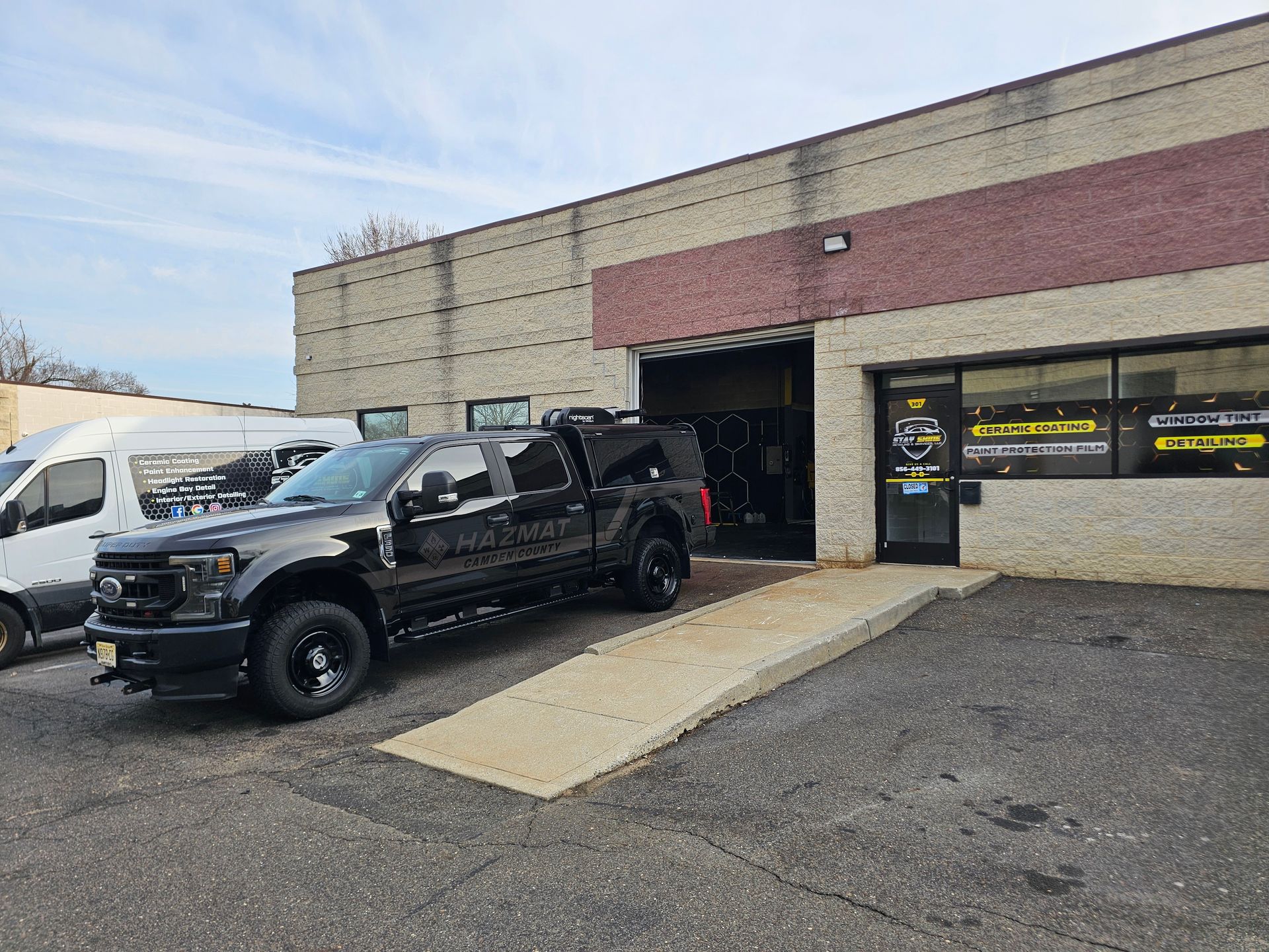 Black truck parked in front of a brick building with open garage door. A ramp leads to the doorway.