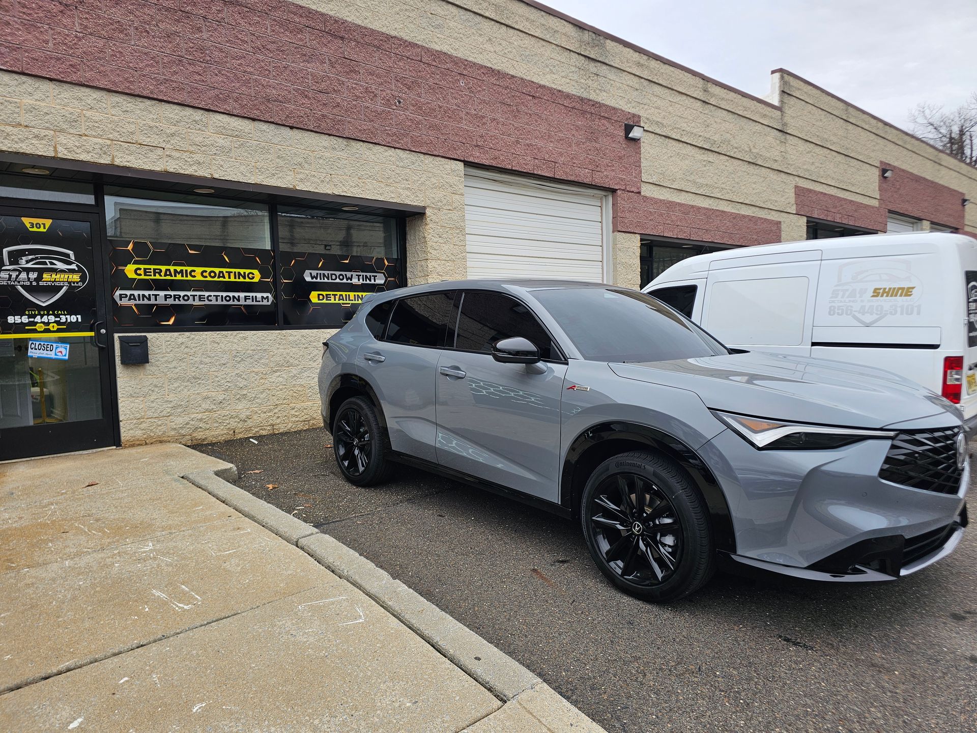 Gray SUV parked outside a brick and tan building with large windows. A white van is visible.