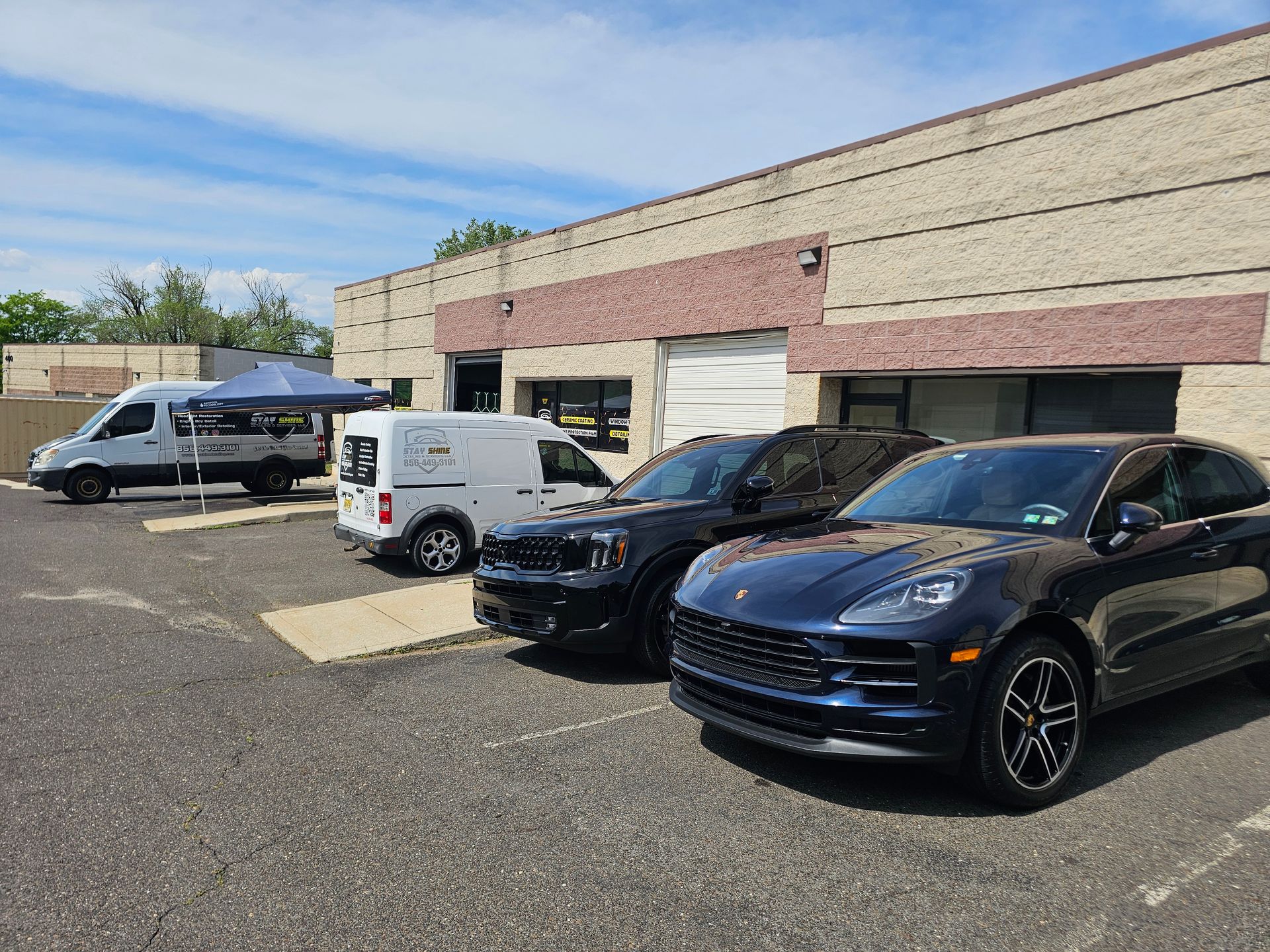 Vehicles parked outside a brick building under a sunny sky; a van and SUVs are visible.