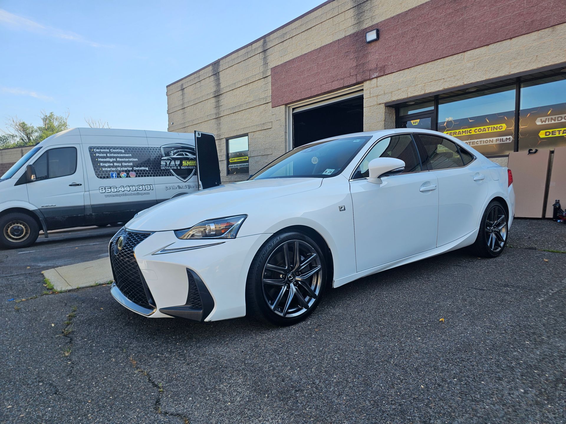 White Lexus car parked outside a building with a van in the background.