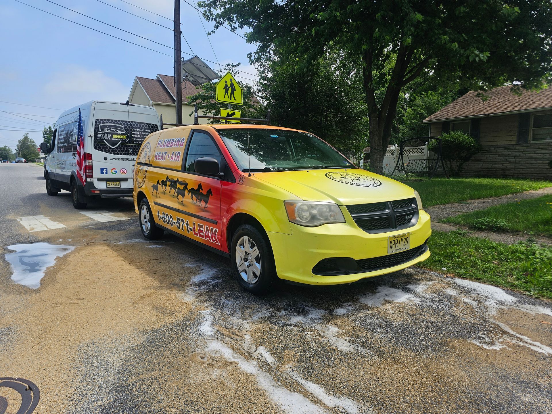 Yellow and red van parked on a street with a bus.  School crossing sign visible. Foam or suds on the ground.