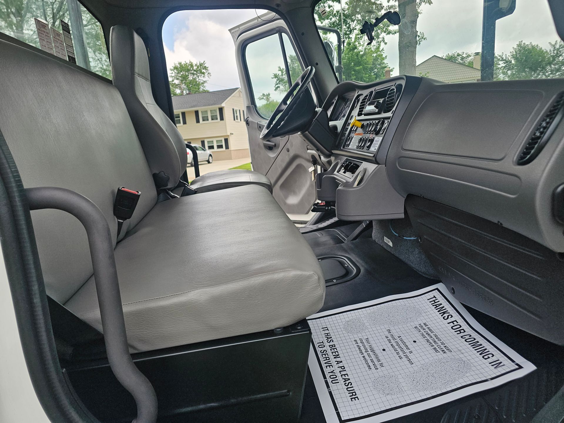 Interior of a white truck cab; gray seats, black dashboard, open door with a residential background visible.