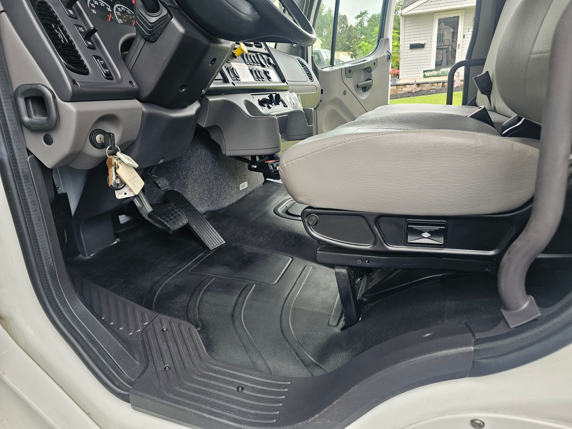 Interior view of a truck cab, showing driver's seat, floor mats, and dashboard in a neutral color scheme.