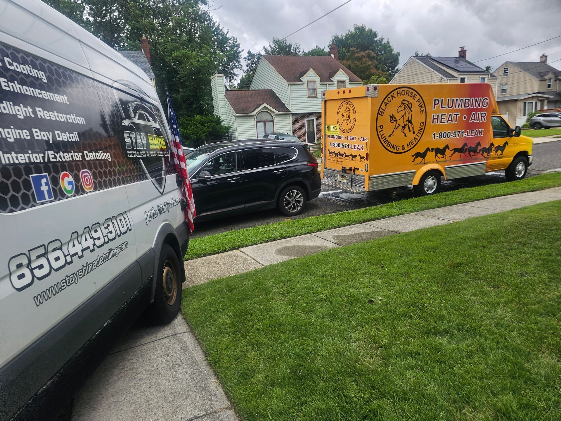 Two service vans parked on a residential street. One van is white, the other yellow. Black car parked between them. Green lawn and houses in background.