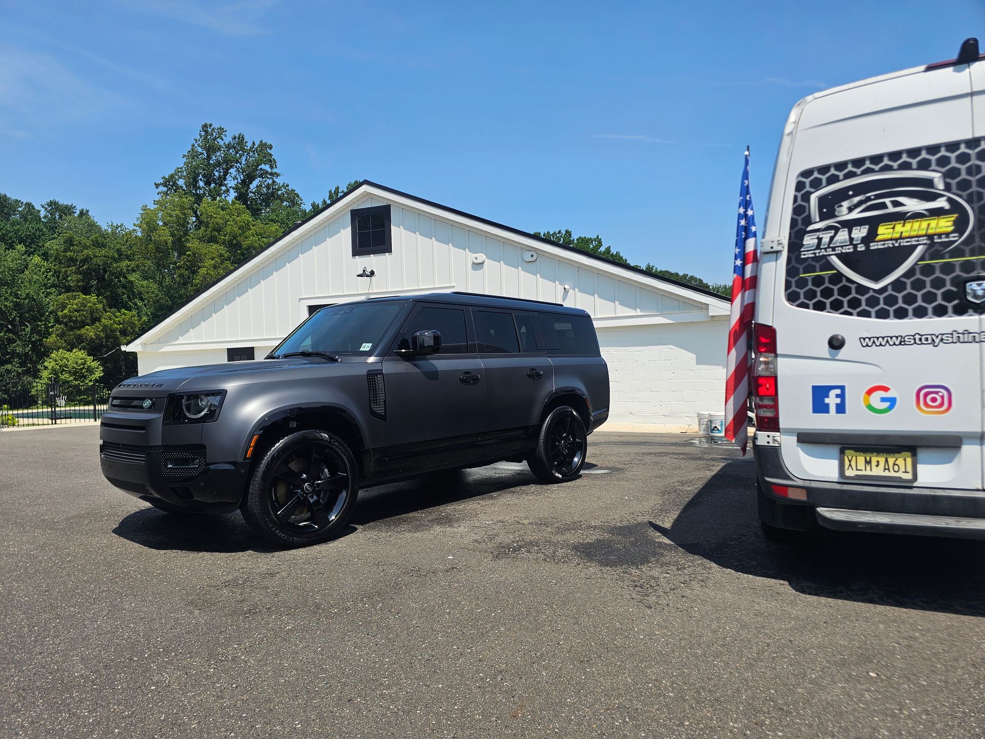 Gray Land Rover Defender parked outside a white building next to a white van on a sunny day.