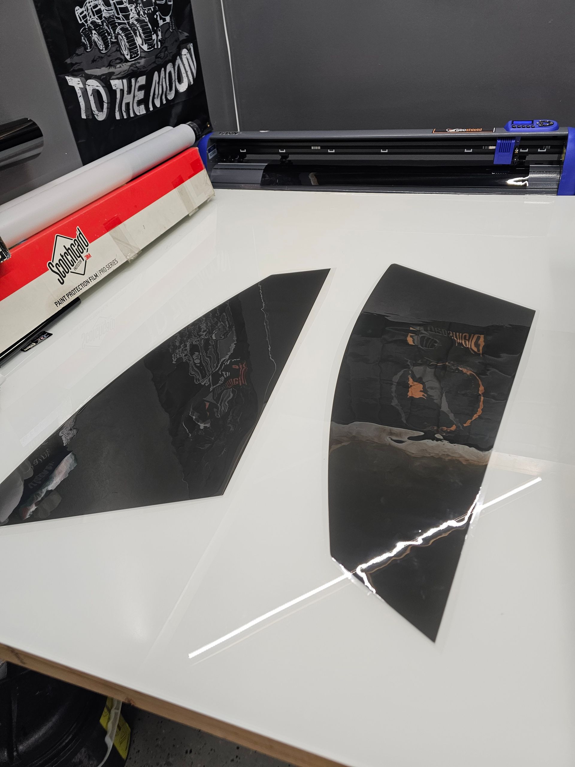 Two tinted car window films on a white table. A red and white box and a black cutter are in the background.
