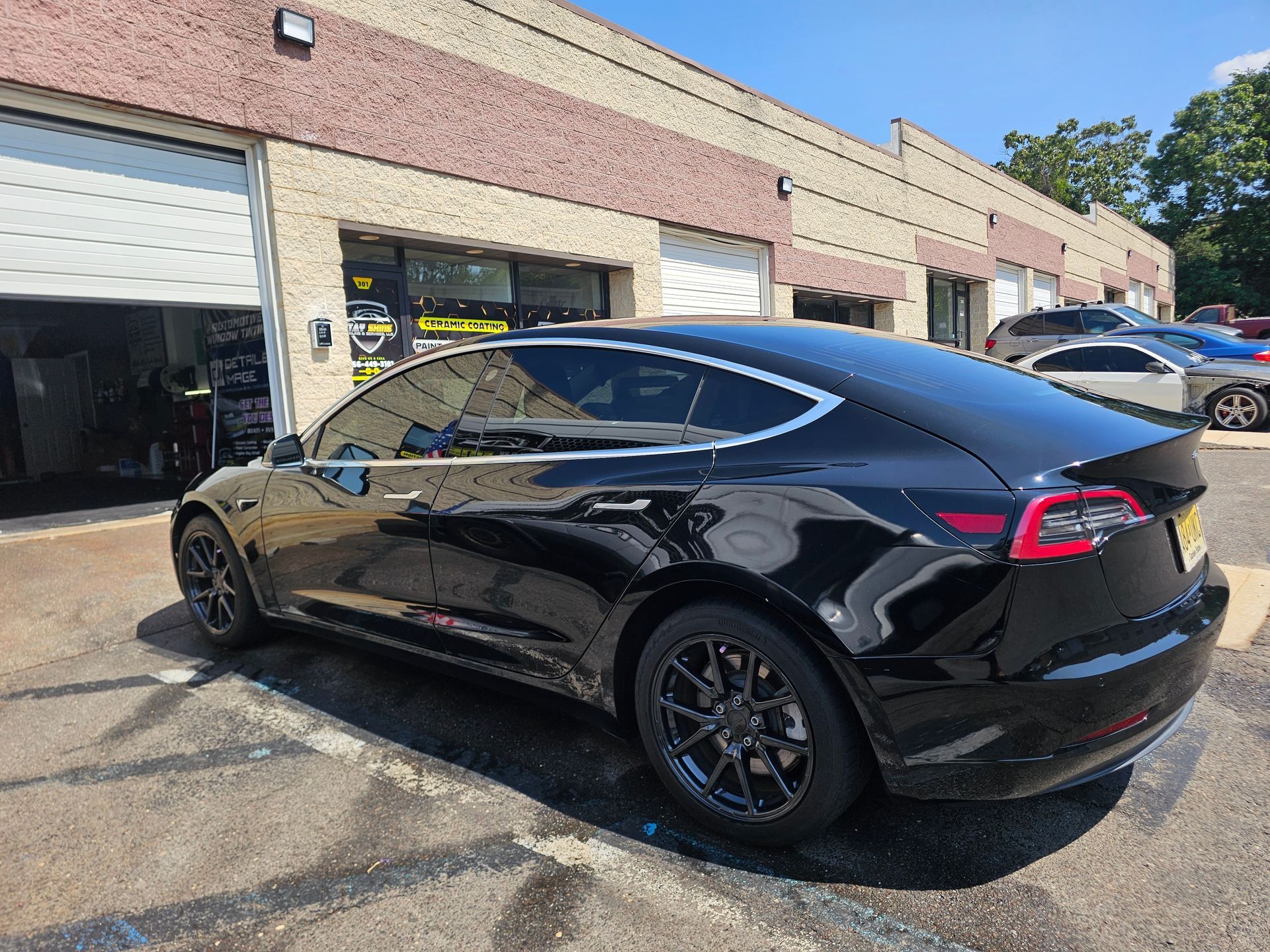 Black Tesla Model 3 sedan parked outside a building with garage bays.