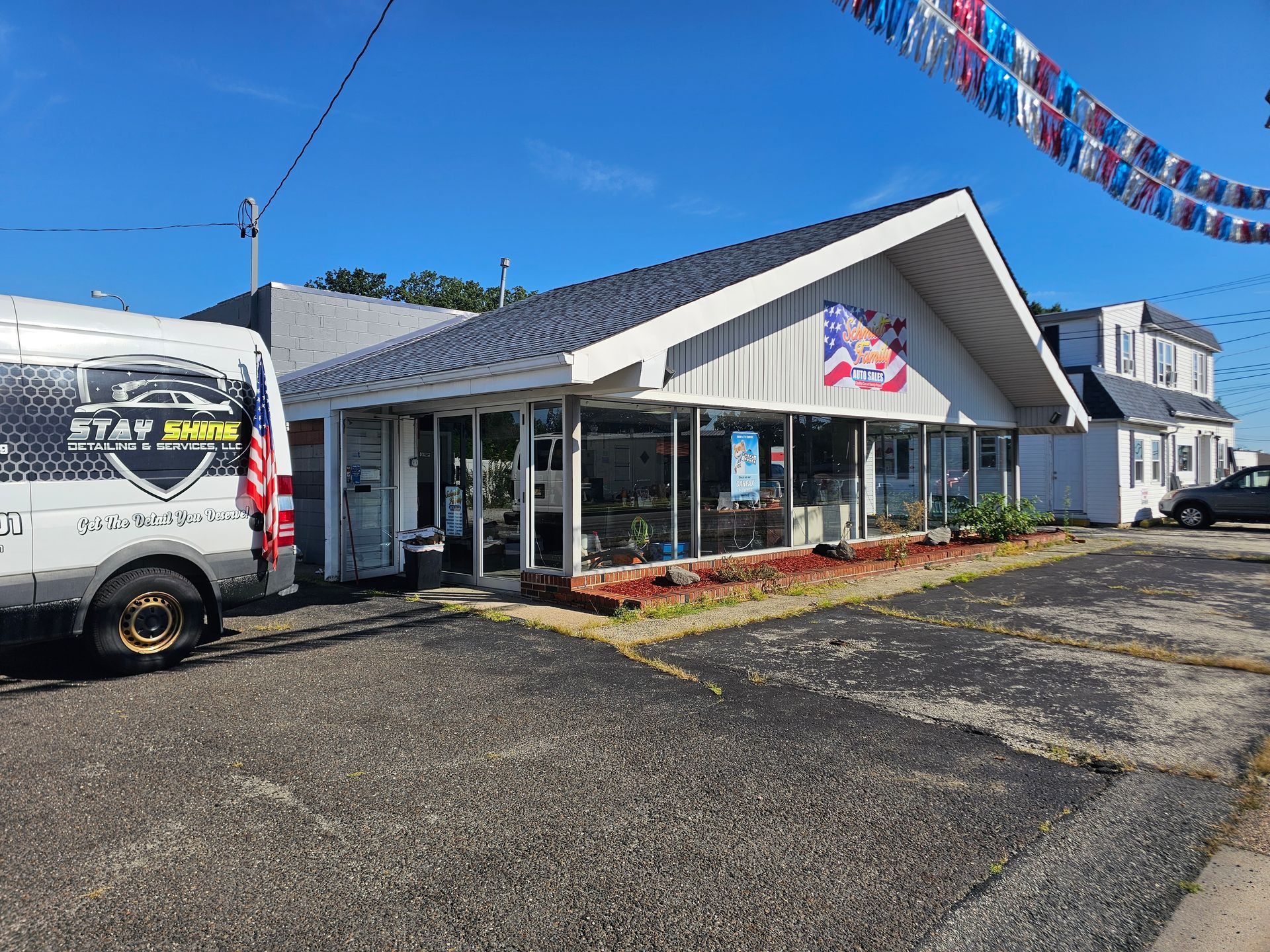 A one-story business building with glass front, van, and US flag under a blue sky.