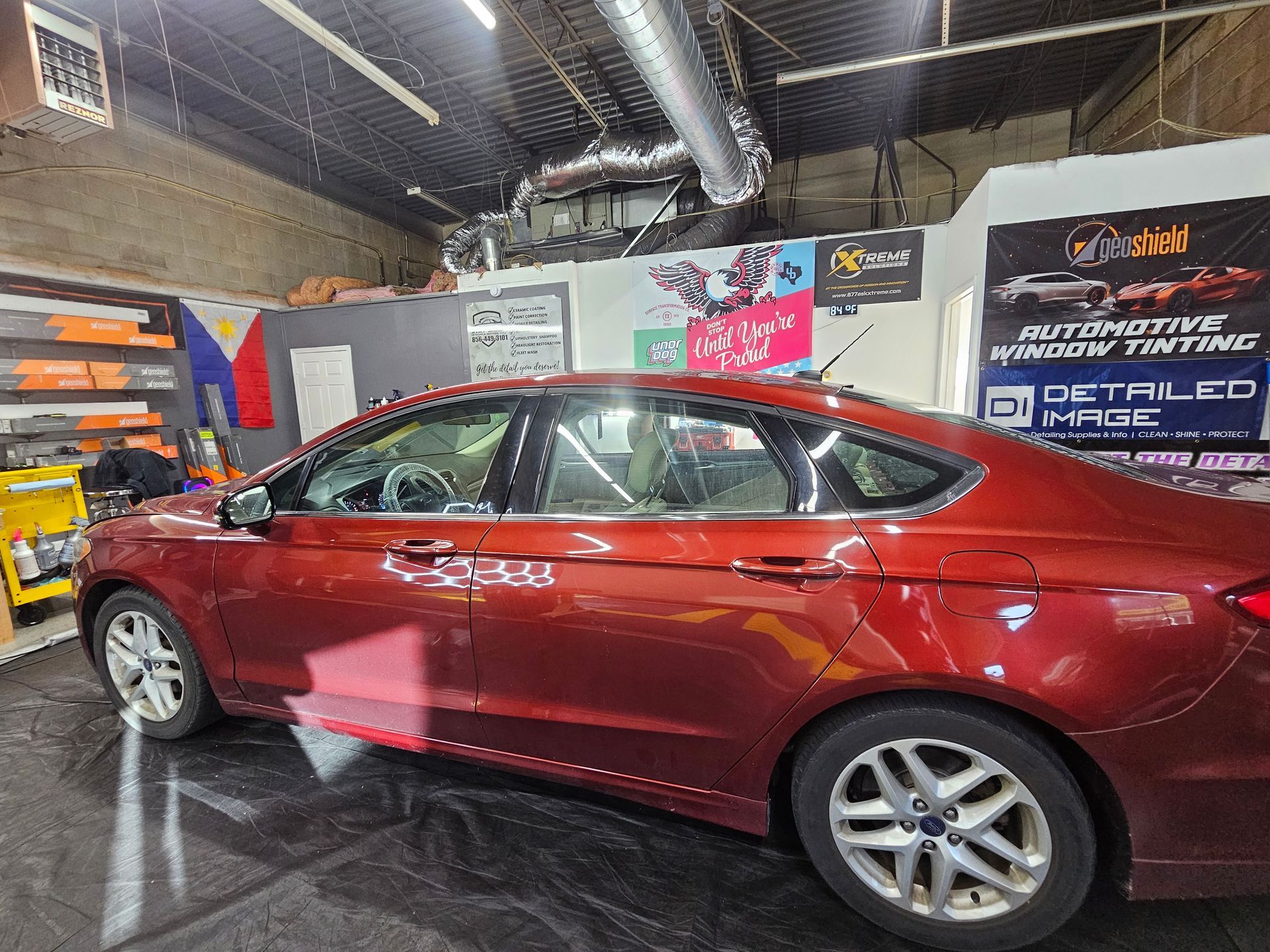 Red sedan in a shop with window tinting signage.