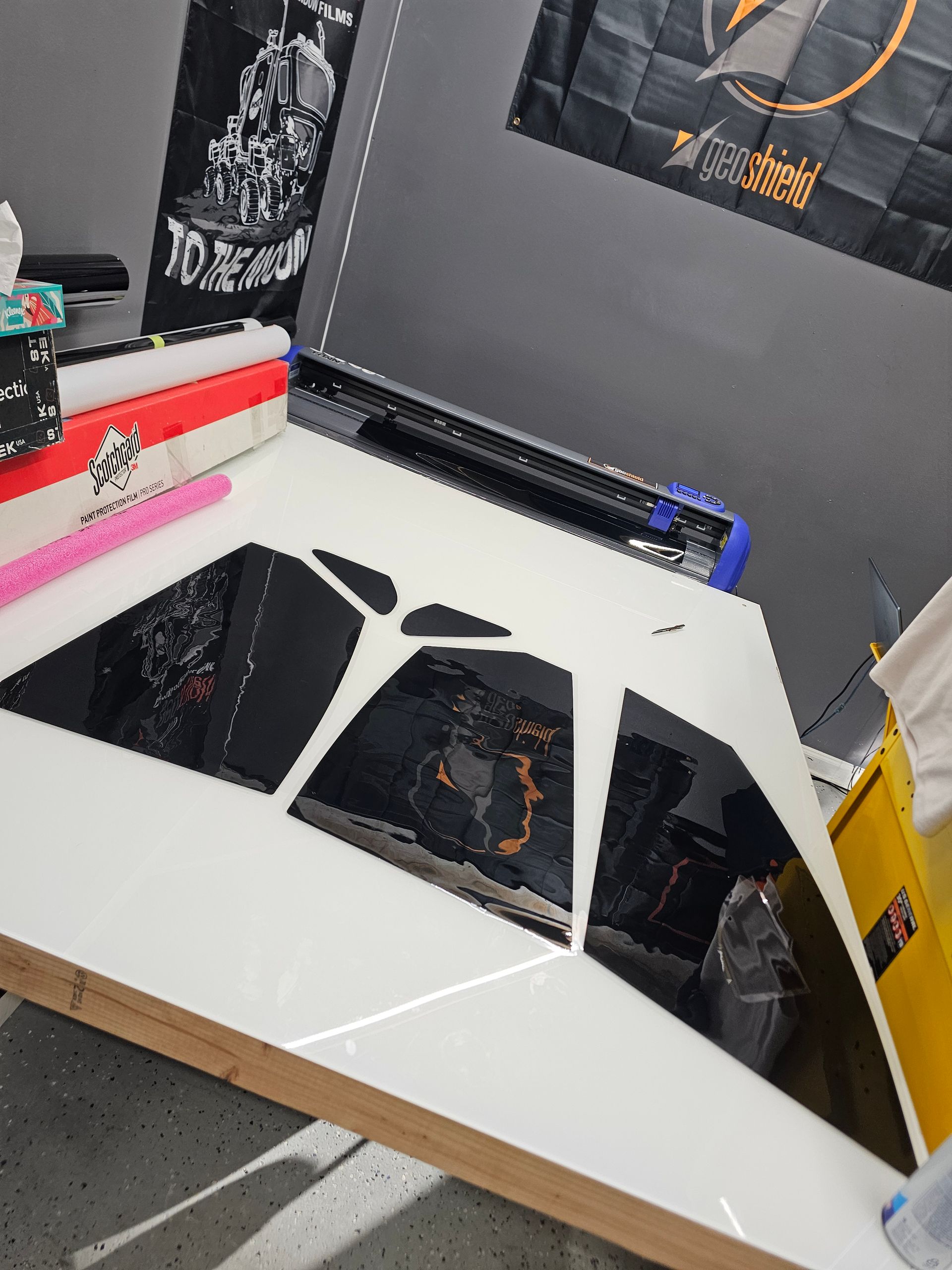 White desk with black triangular vinyl shapes, with vinyl roll and cutting machine, indoors.