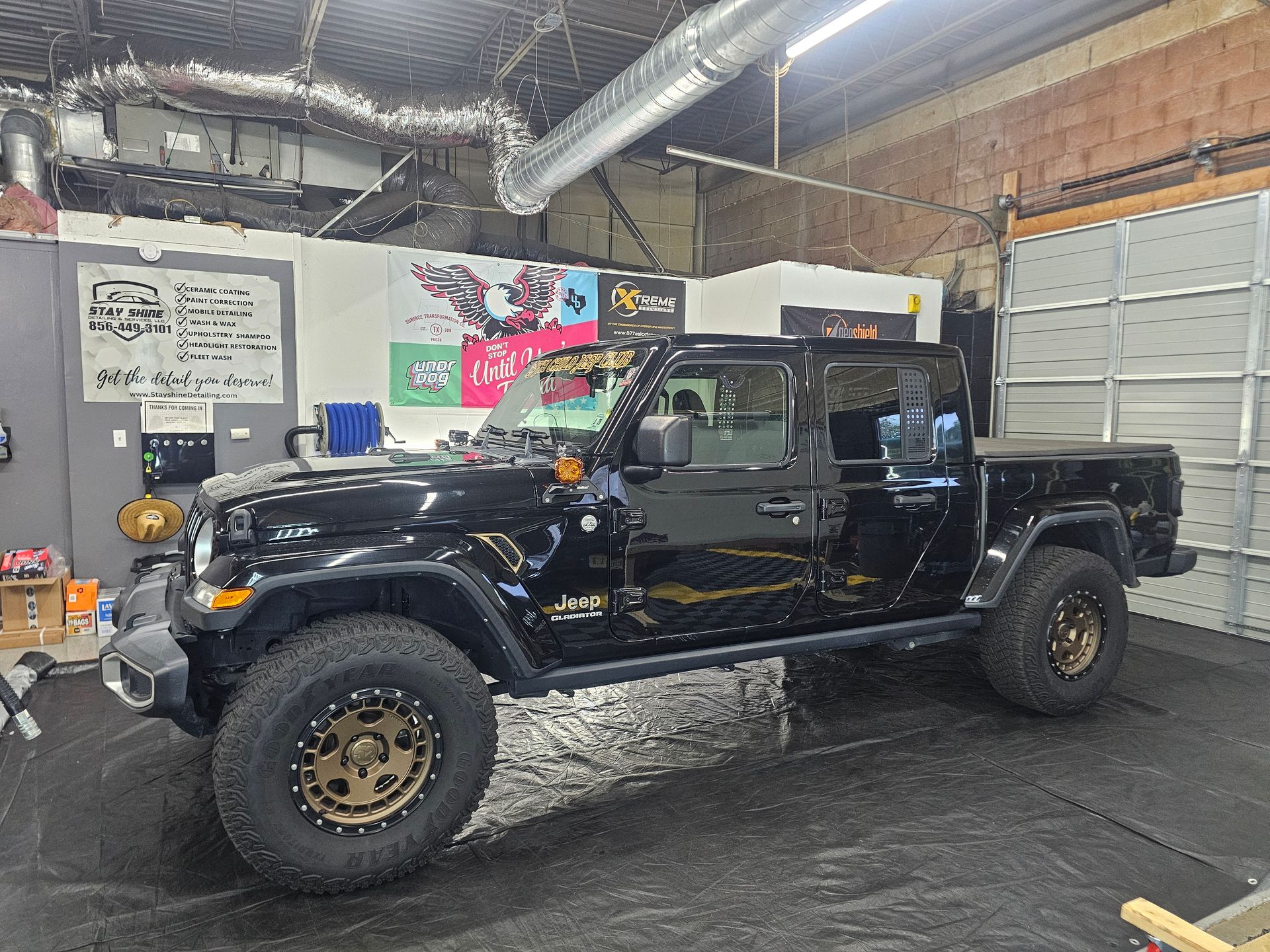 Black Jeep Gladiator truck with bronze wheels inside a garage.